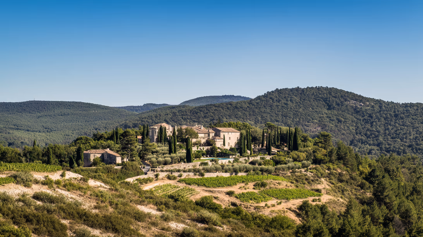 Landschap met een landhuis temidden van cipressen en wijngaarden, omgeven door groene heuvels onder een heldere blauwe lucht.