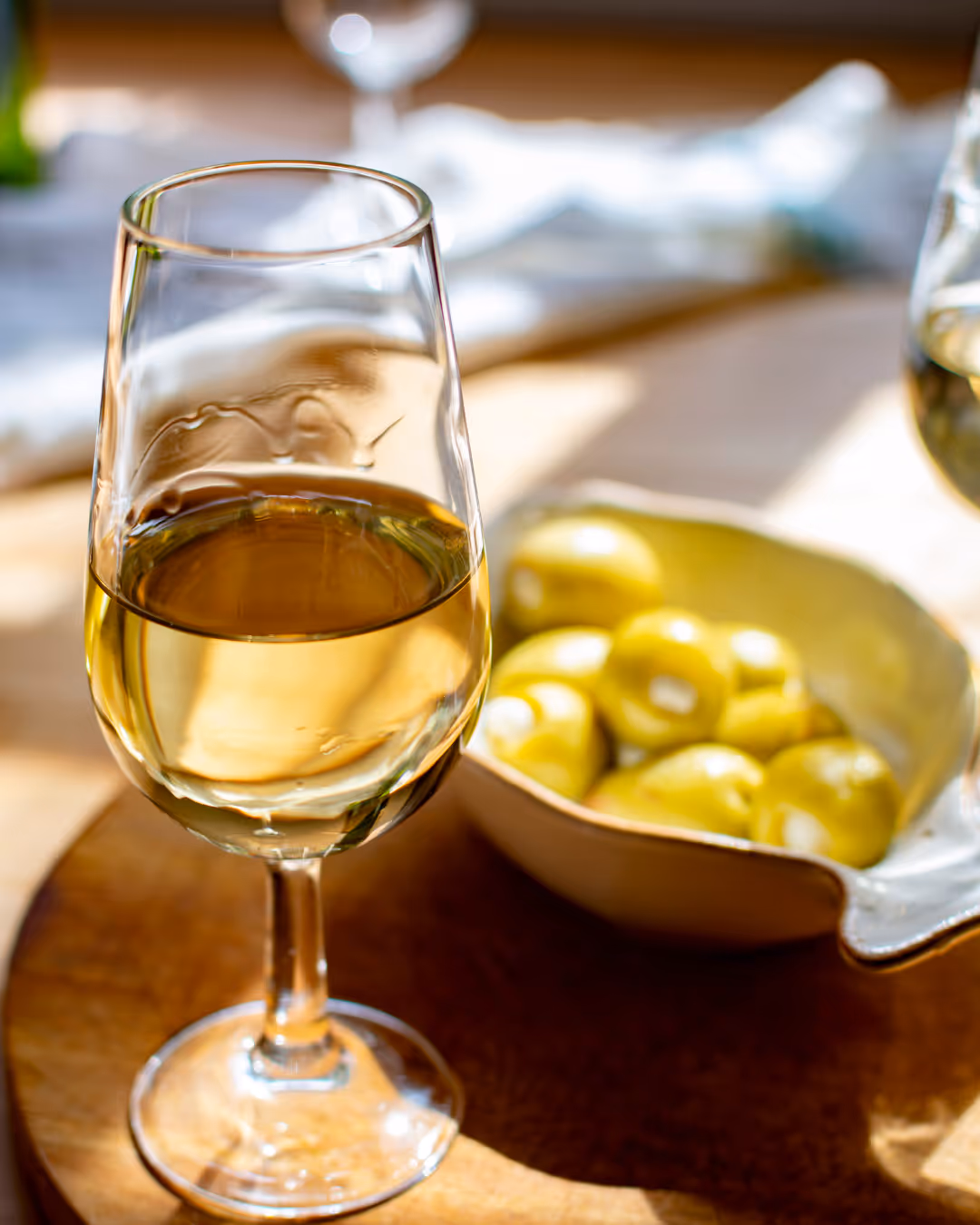 Glas witte wijn op een houten tafel naast een schaal met groene olijven.