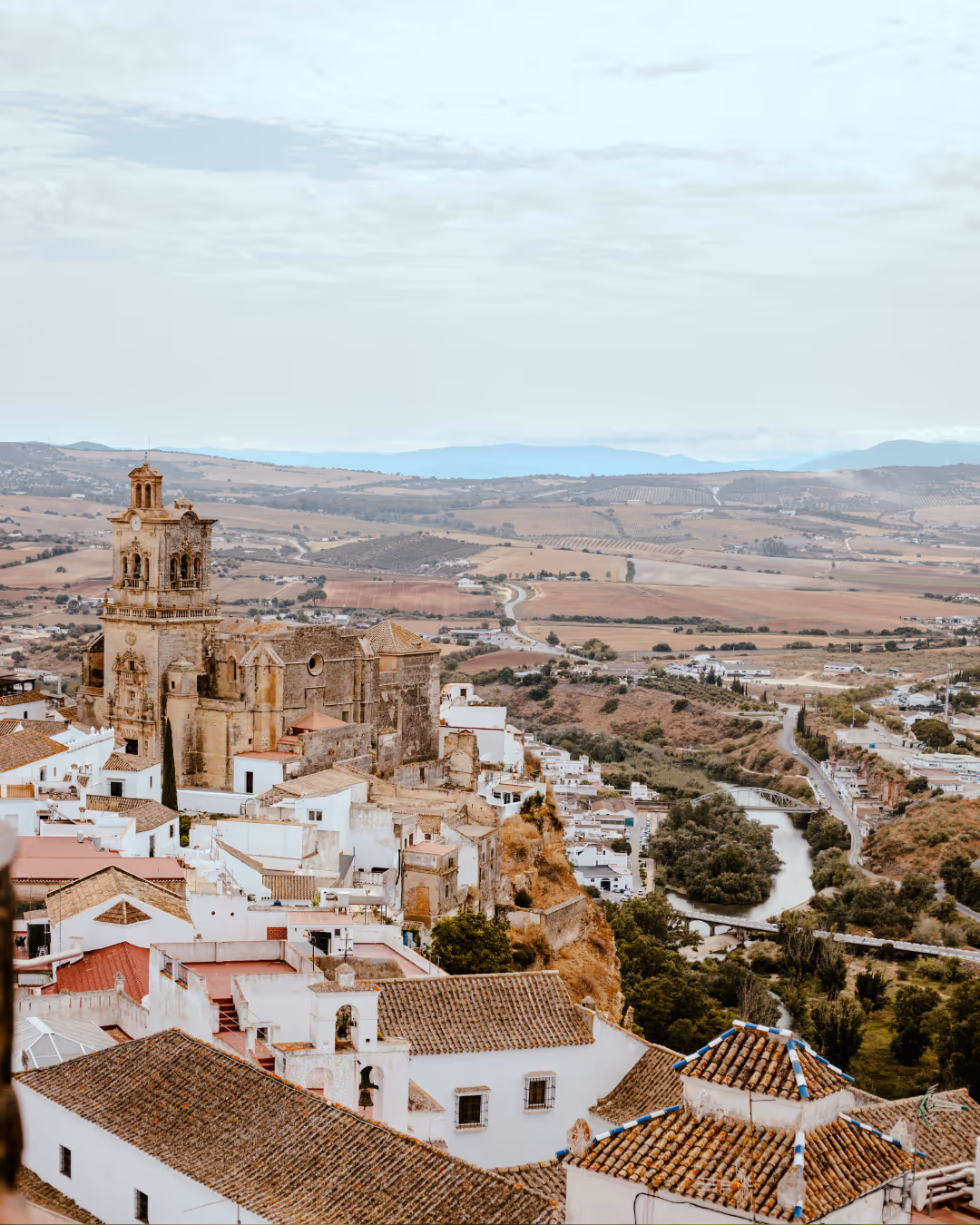 Uitzicht over witgekalkte huizen met terracotta daken en een oude kerk aan een rivier in een landelijke vallei.