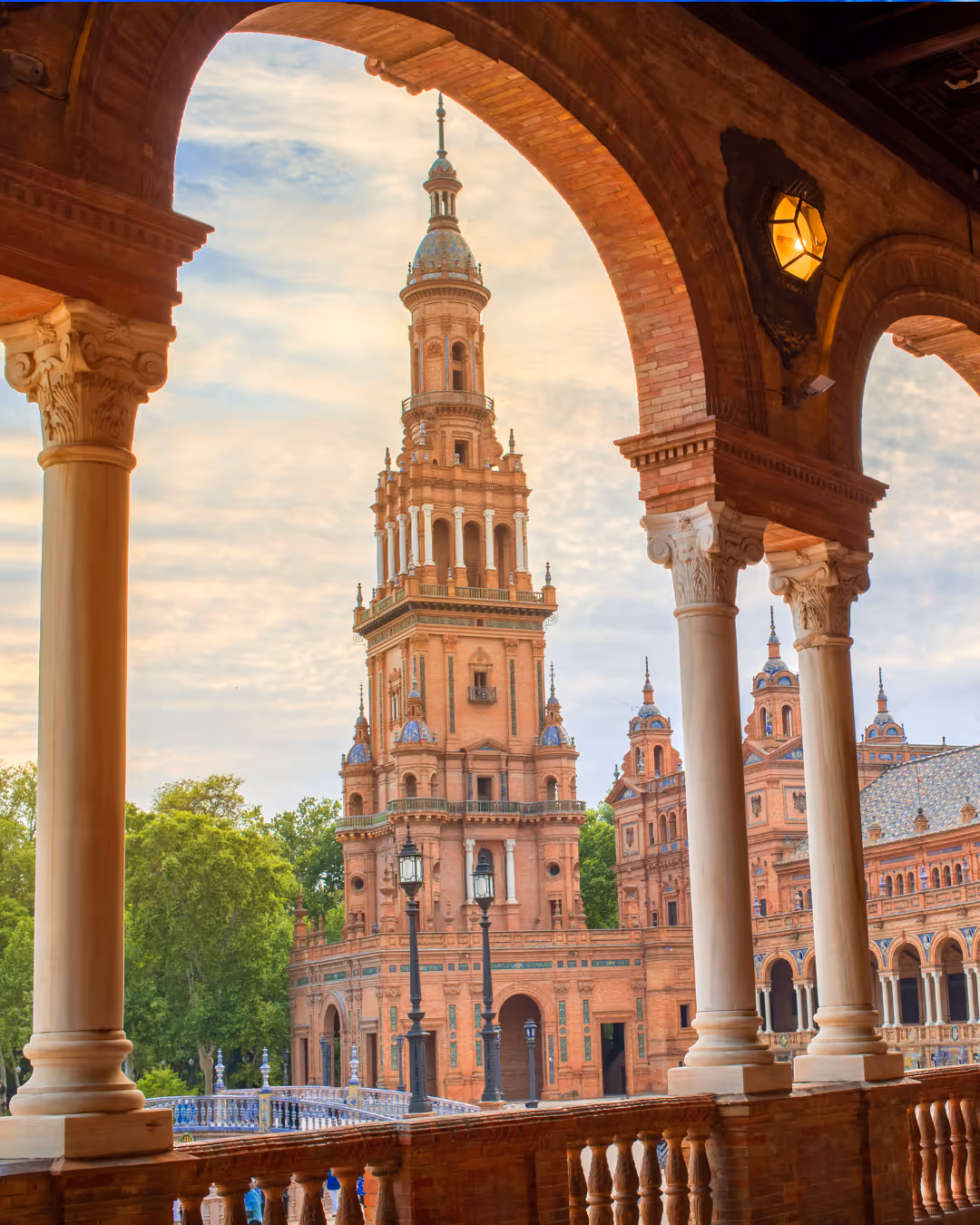 Uitzicht op de toren van het Plaza de España in Sevilla, geframed door bogen en zuilen van een galerij.