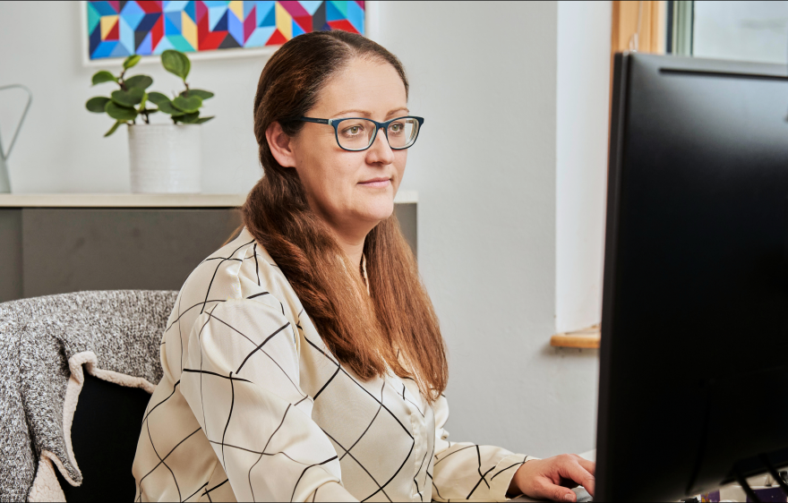 Finanzbuchhalerin mit Brille, die an einem Schreibtisch vor einem Computerbildschirm sitzt und konzentriert arbeitet.