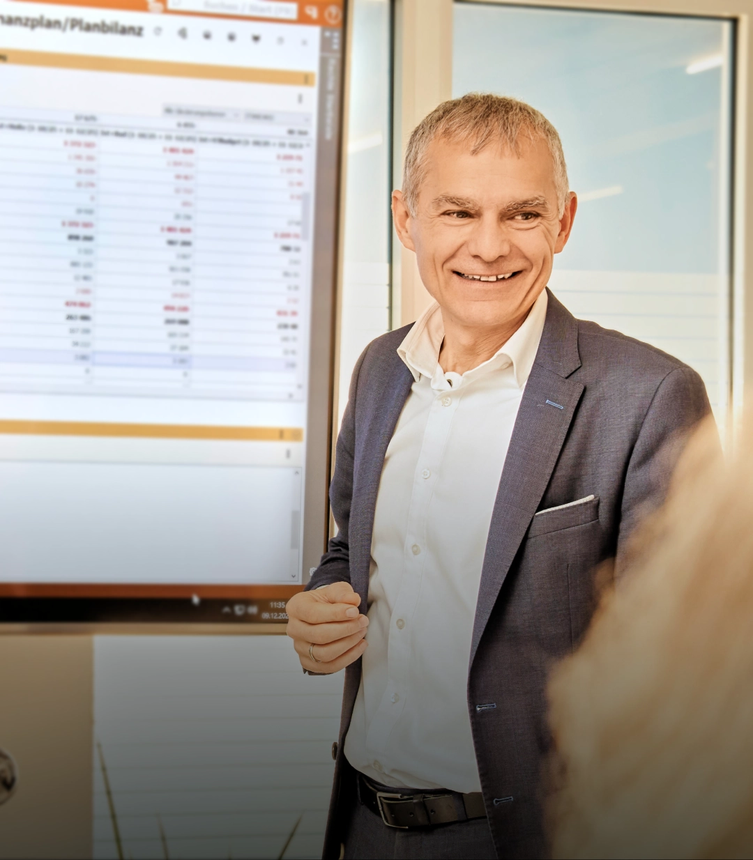 Walter Aigner-Glösl gibt eine Präsentation vor einem Bildschirm mit Finanzdaten in einem modernen Büro.