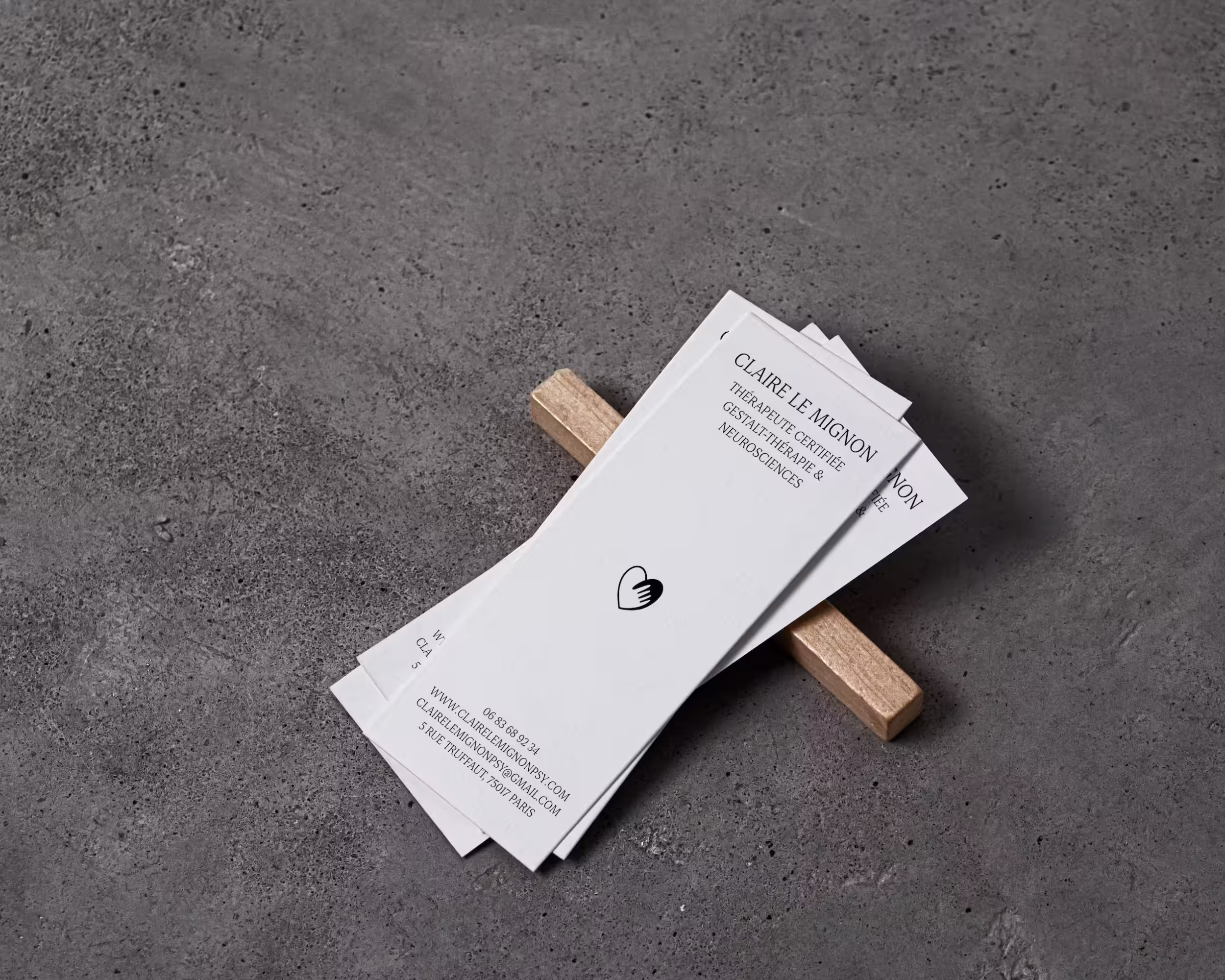 Cartes de visite blanches empilées avec nom Claire Le Mignon, thérapeute certifiée en gestalt-thérapie et neurosciences, posées sur surface grise avec pince en bois.