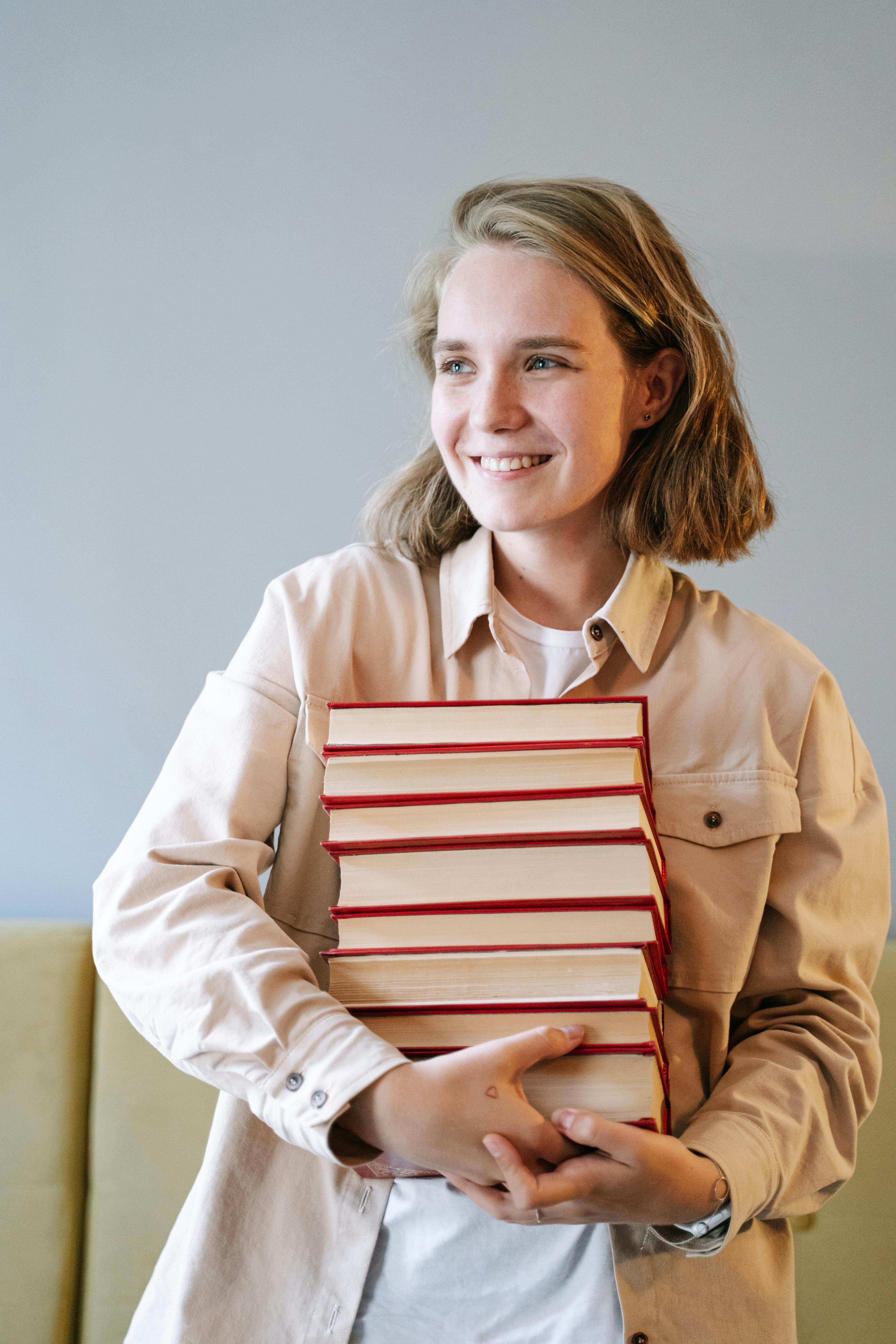 Smiling young woman holding a stack of seven hardcover books with red spines.