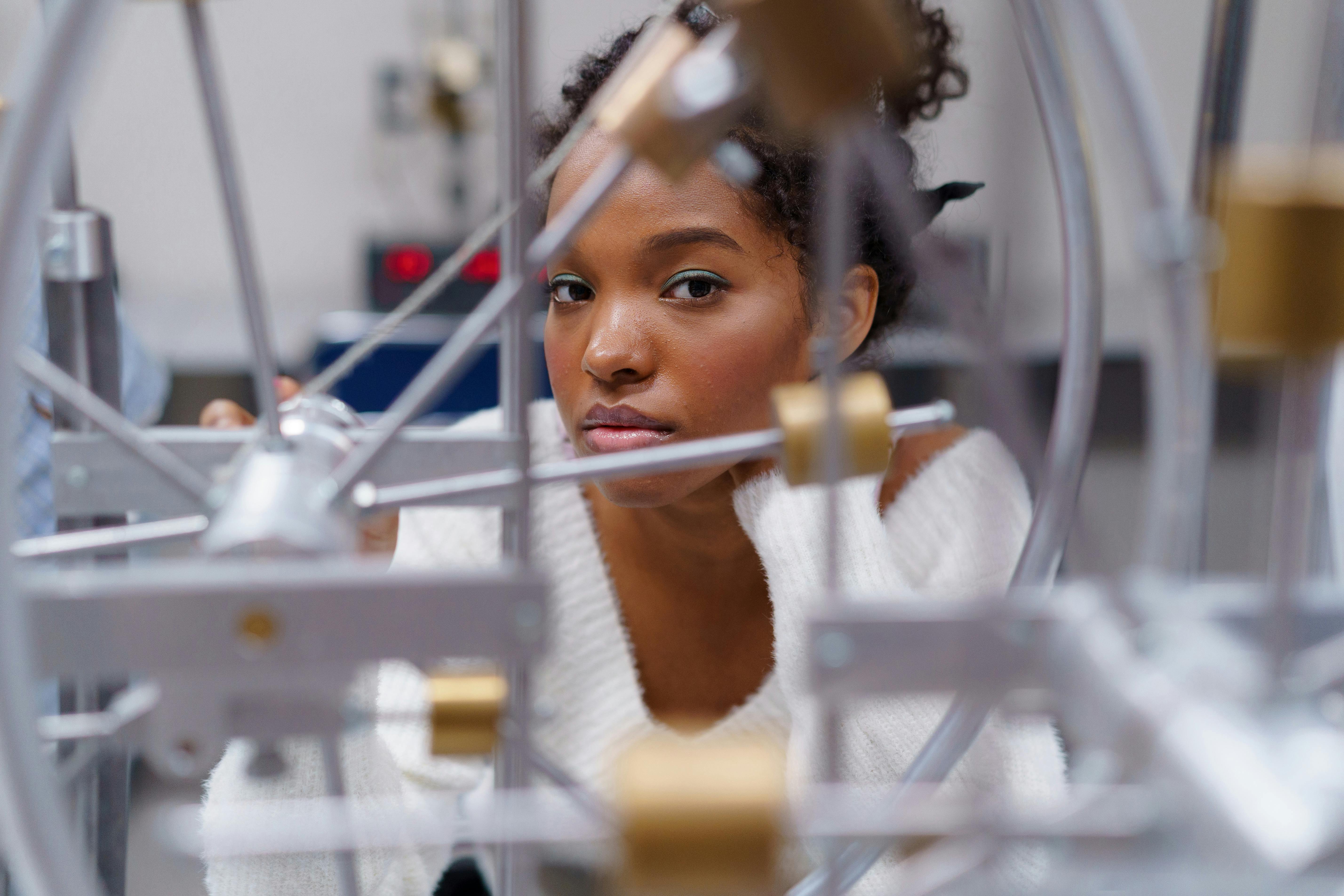 Young woman in a white sweater observing and working on a complex mechanical device with gears.