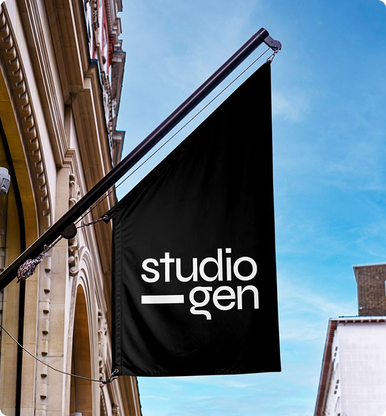 Black rectangular hanging banner with white text 'studio gen' attached to a pole on a building exterior under a blue sky.
