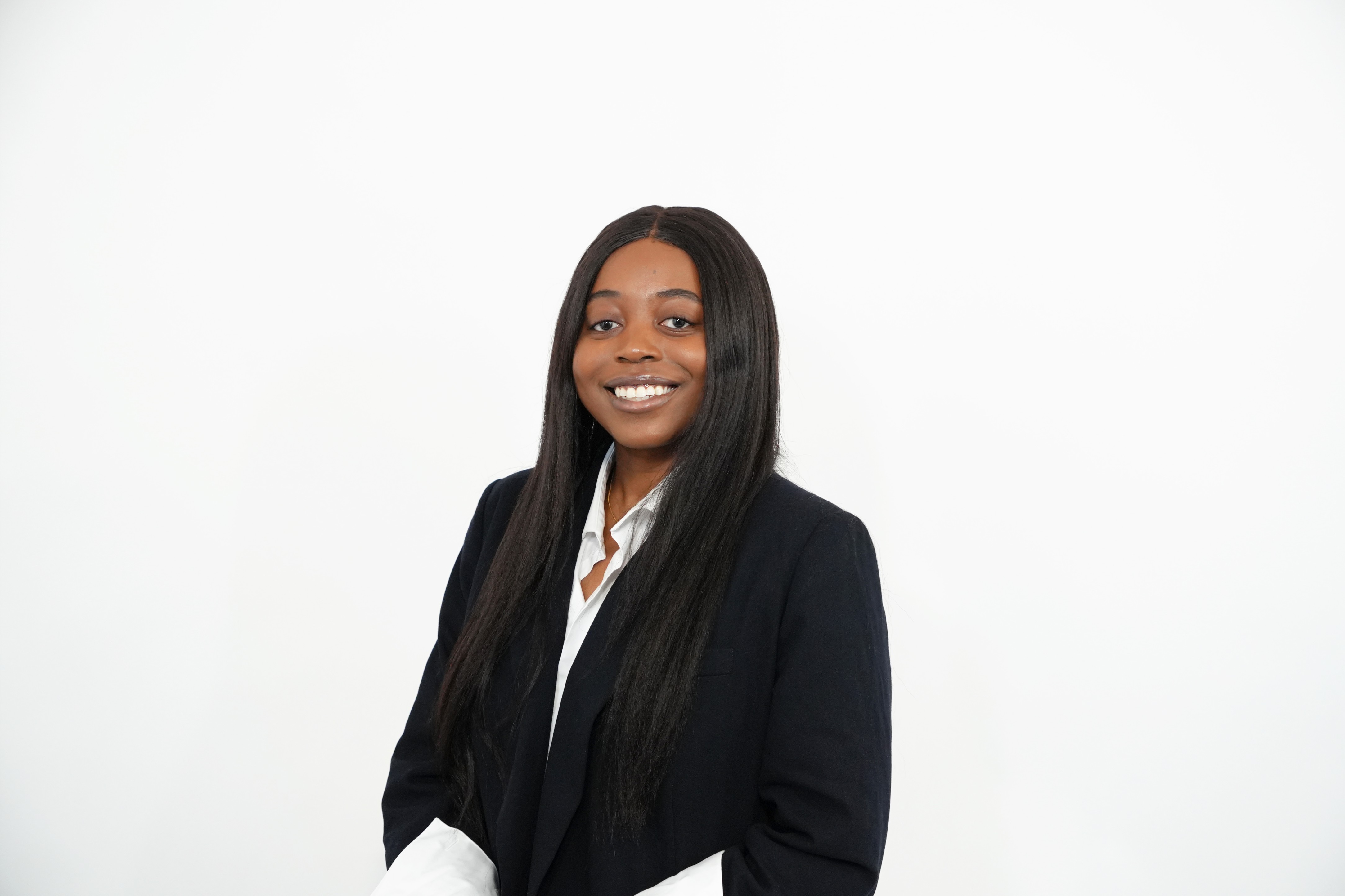 Smiling woman with long straight hair wearing a black blazer and white shirt against a white background.