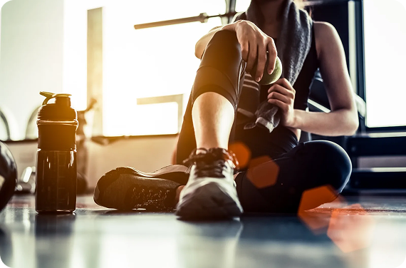 Woman sitting on the gym floor resting after a workout with a water bottle nearby