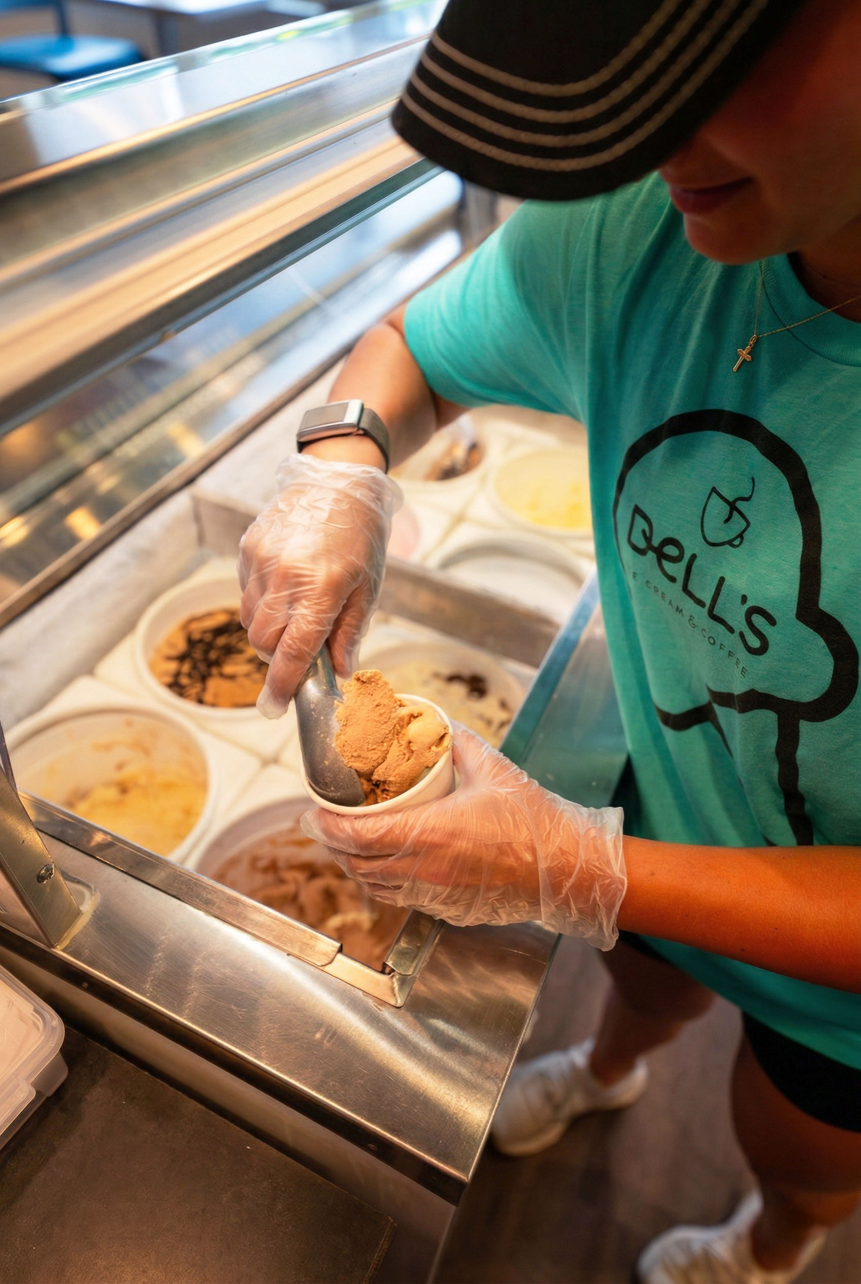 Person scooping chocolate ice cream into a cup at an ice cream shop wearing a Bell's Cream & Coffee shirt.