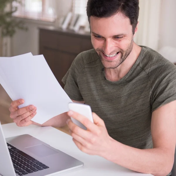 A man seated at a table, working on a laptop with a sheet of paper beside him.