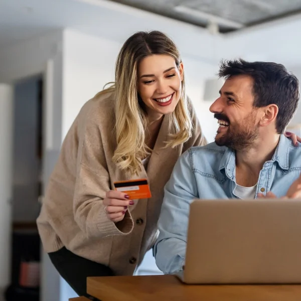 Couple sitting together, using a credit card to make an online purchase on a laptop.