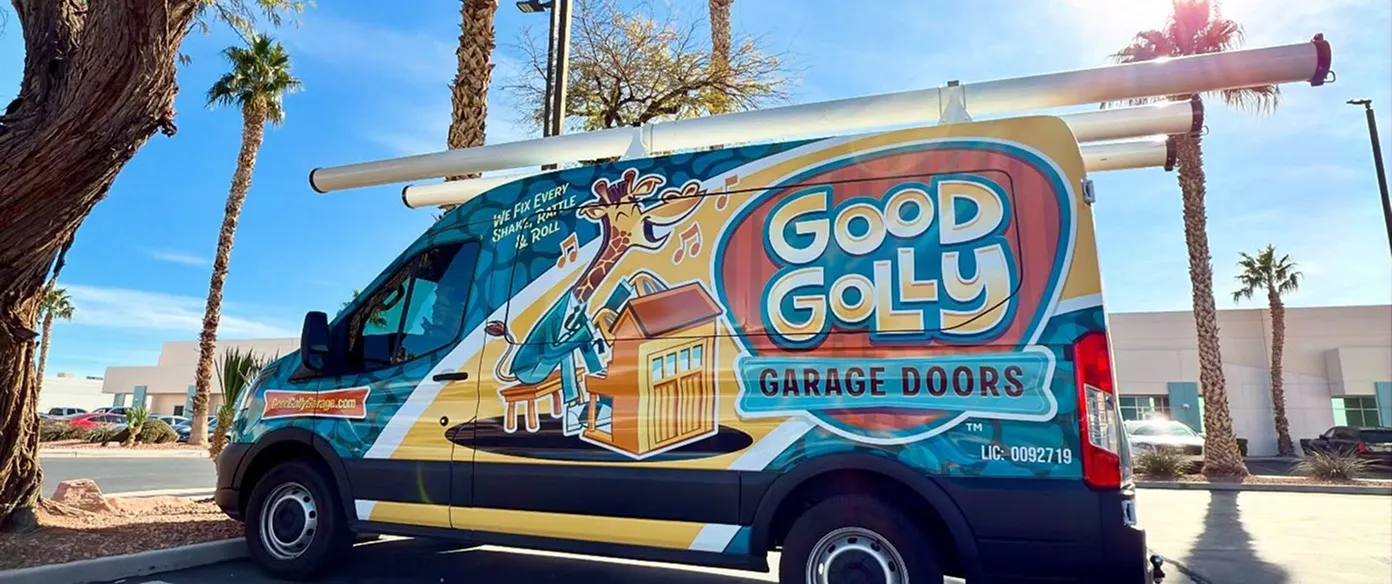 Blue and yellow Good Golly Garage Doors van with a cartoon giraffe playing piano and carrying garage door parts, parked outdoors near palm trees under a clear sky.