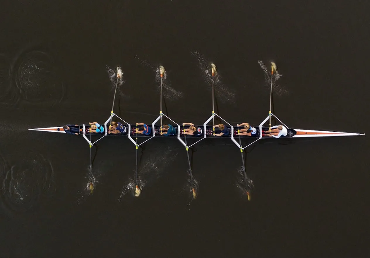 Luchtfoto van een roeiteam van acht personen dat hun slagen synchroniseert op donker water.