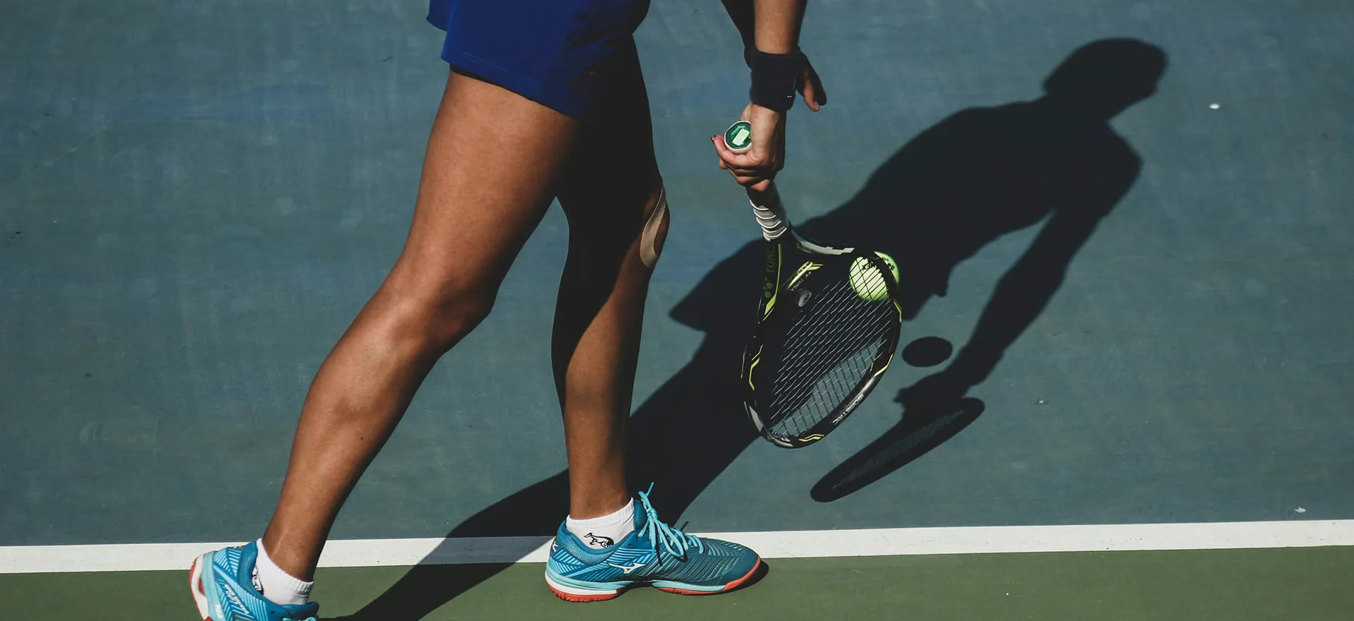 Een tennisser in blauwe schoenen en korte broek maakt zich klaar om een tennisbal met een racket te slaan op de tennisbaan.