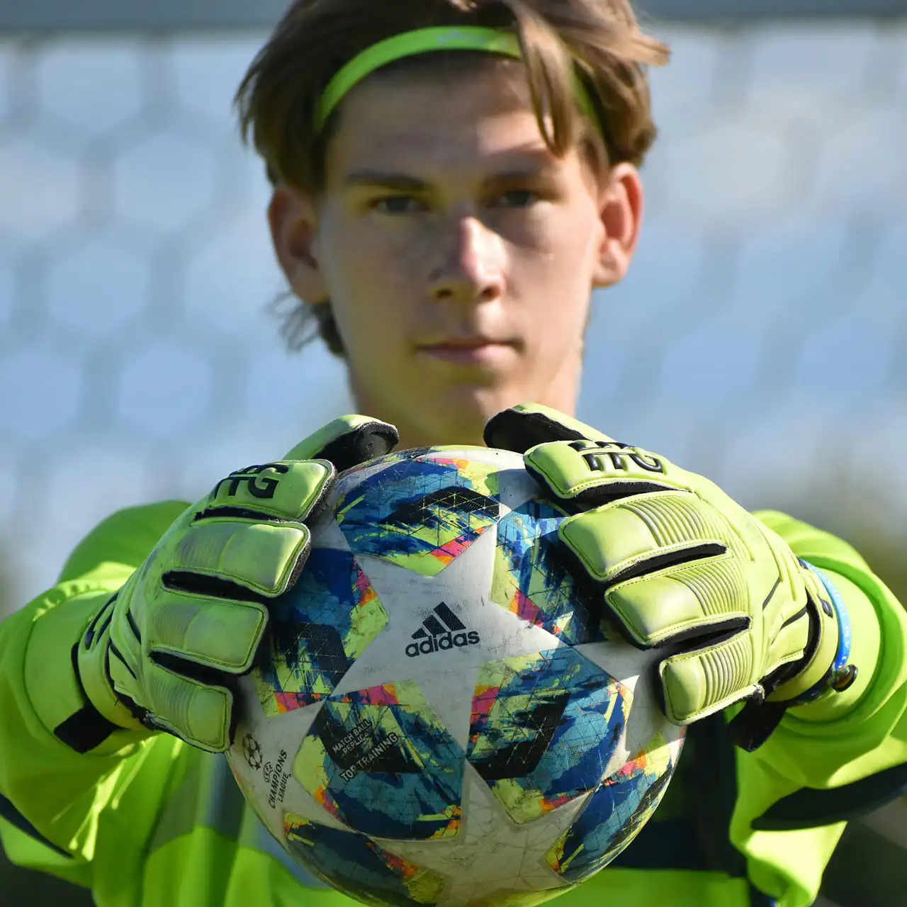 Jonge zelfverzekerde keeper houdt voetbal stevig vast met keepershandschoenen.