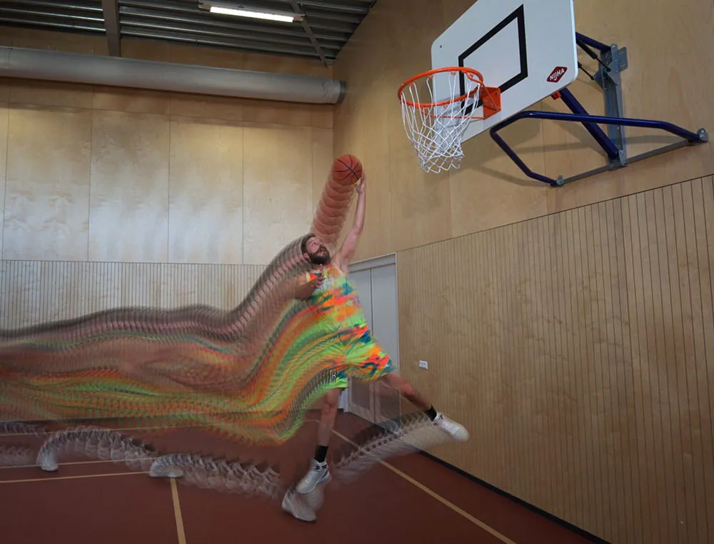 Een mannelijke basketballer springt voor een lay-up op een indoor basketbalveld.
