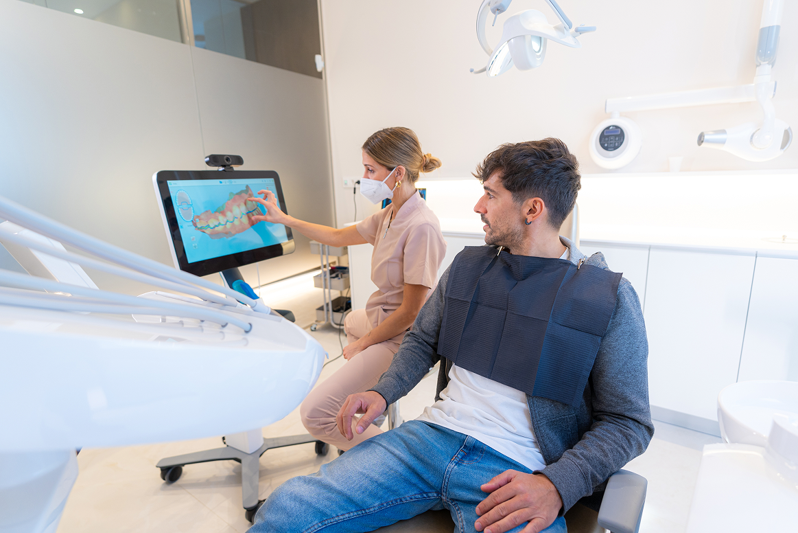 A dentist shows a patient a dental scan on a screen, both seated in a modern office.