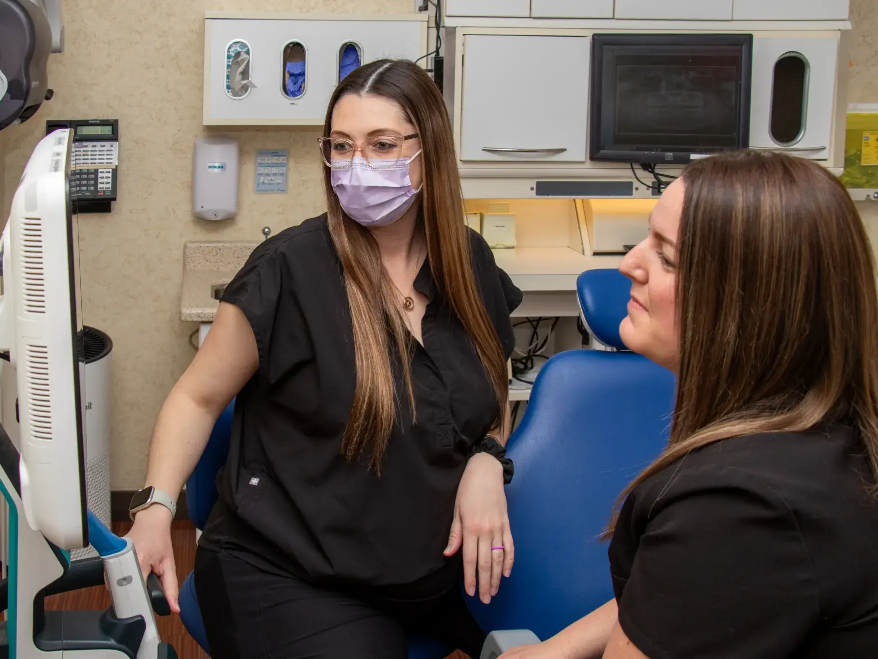 A patient lies in a dental chair while two dental professionals prepare tools.