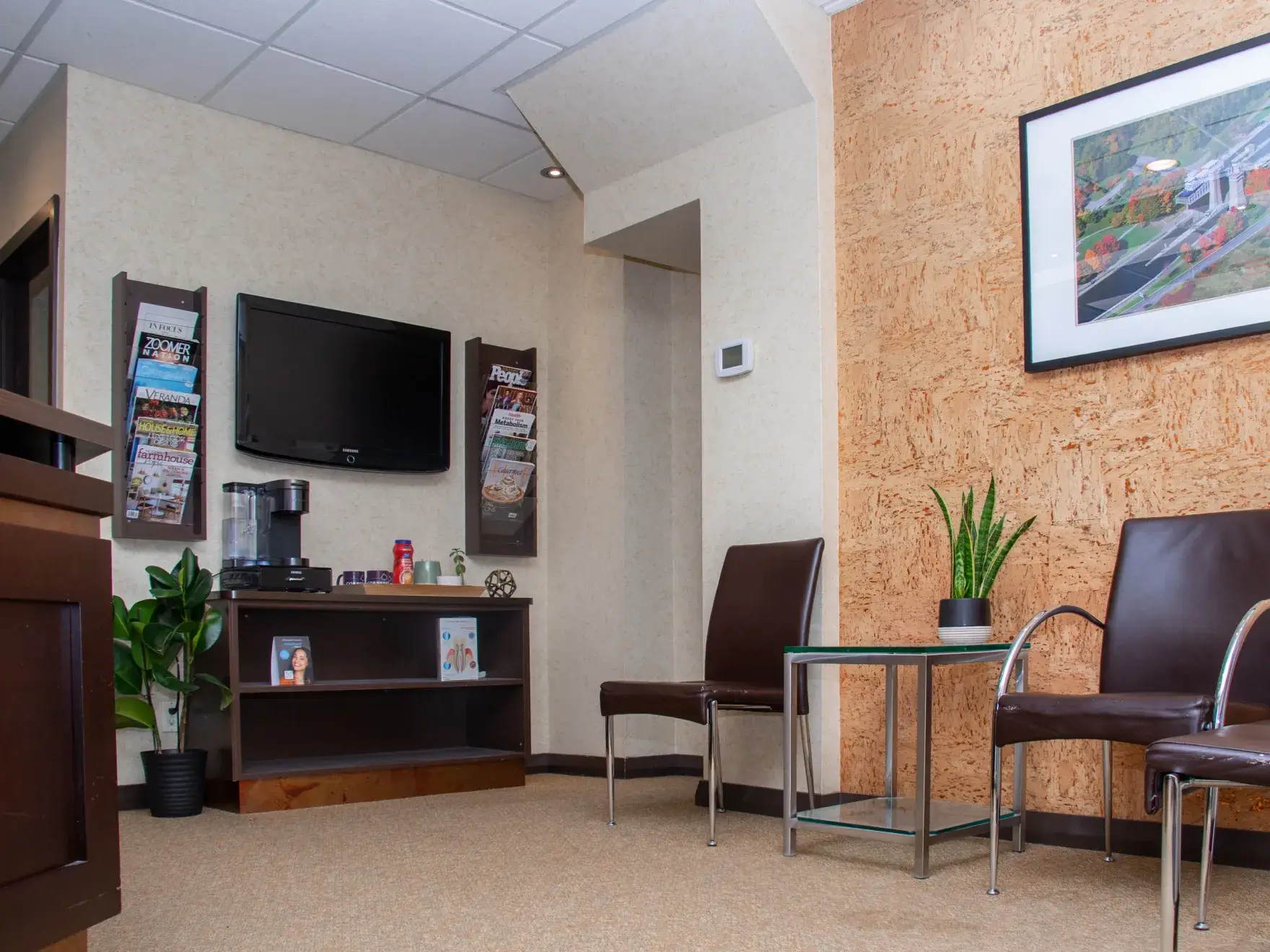 Waiting room with brown chairs, a TV, magazines on the wall, and a small coffee station.