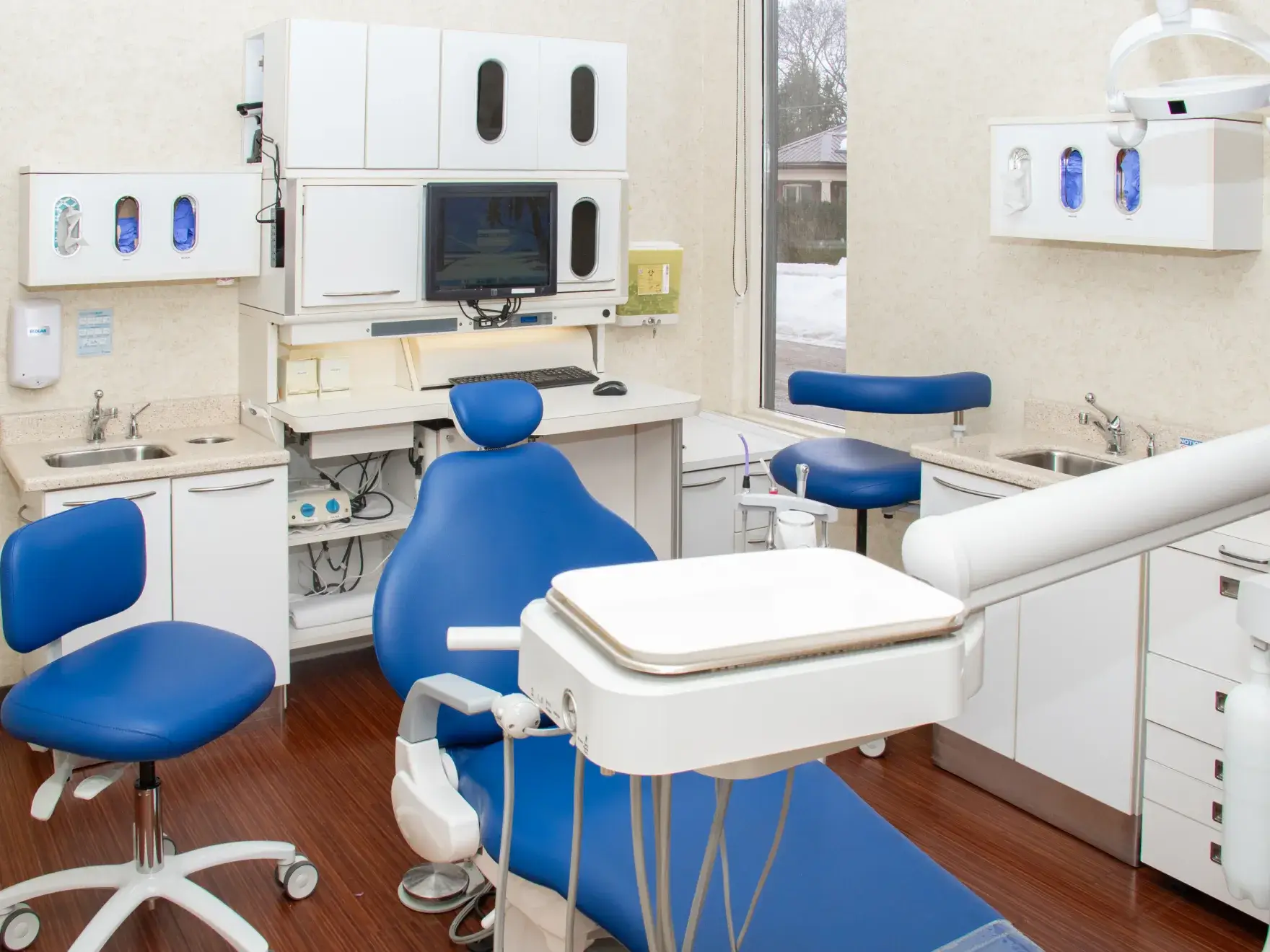 A clean, modern dental office with a blue dental chair and equipment surrounding it.