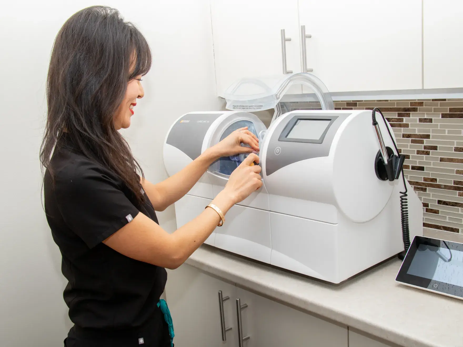 A woman operates a dental milling machine in a clinic setting.