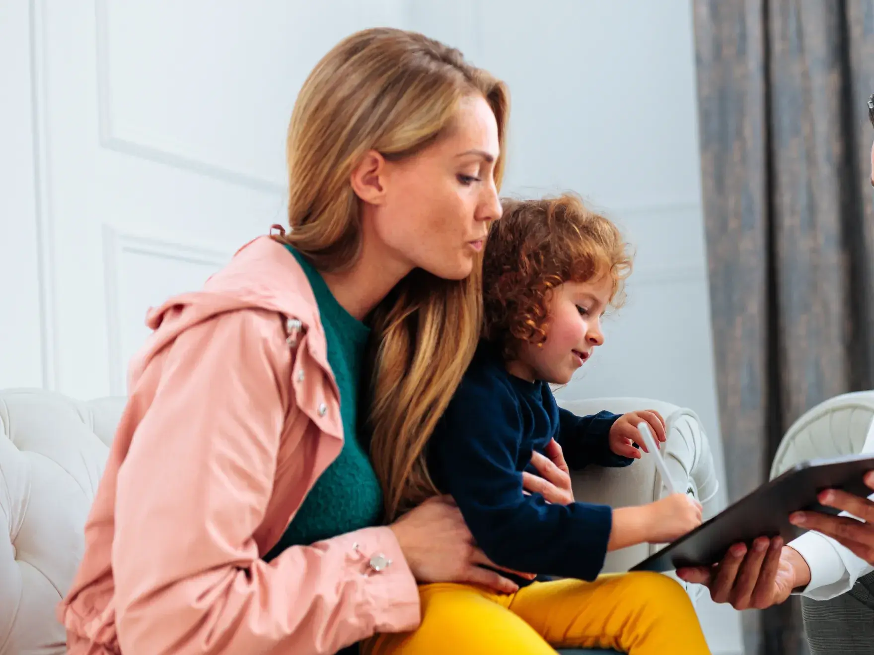 A woman and a child look at a tablet together while sitting on a couch.