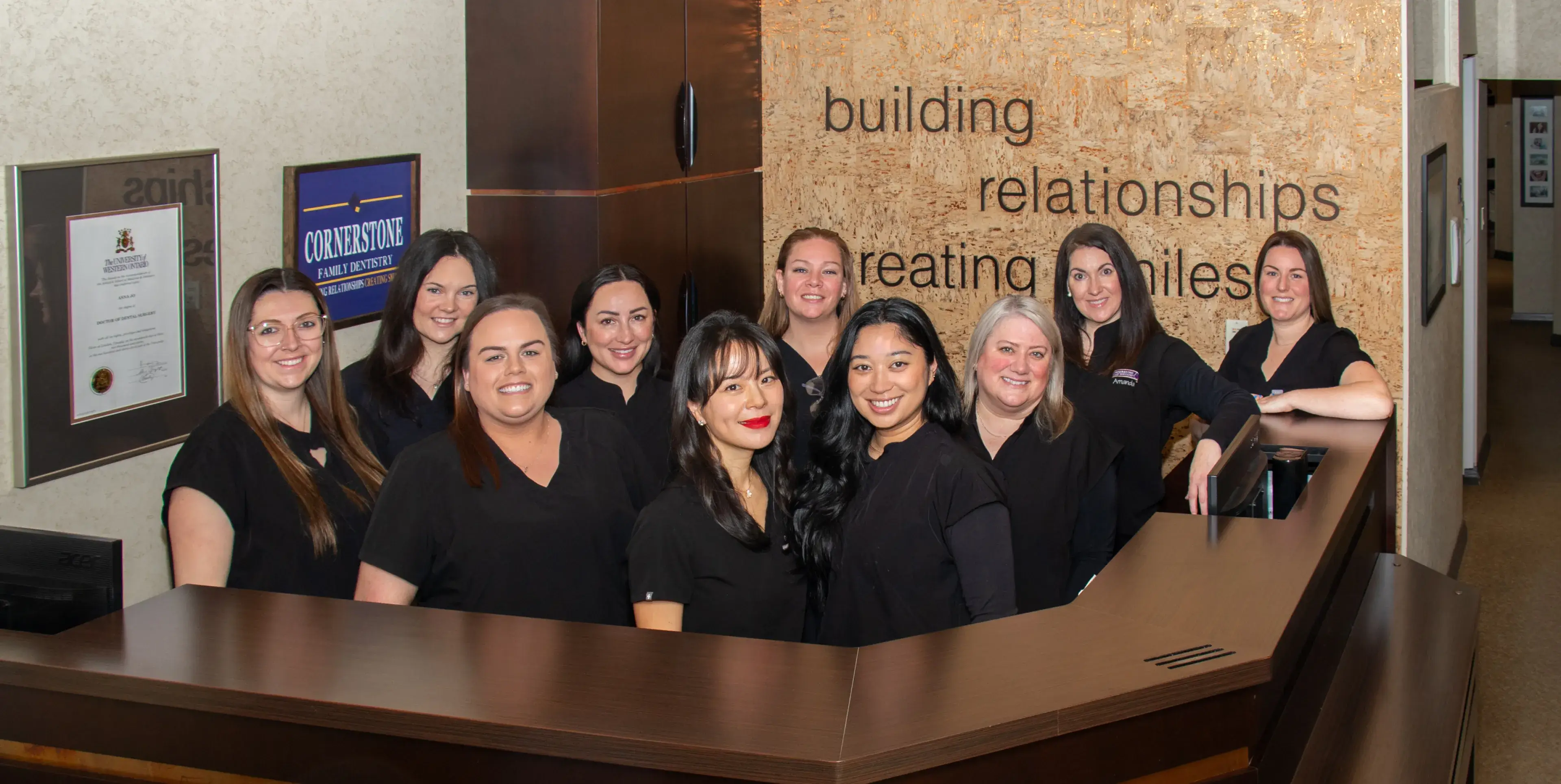 A group of eleven people in black attire smiling and standing behind a reception desk.
