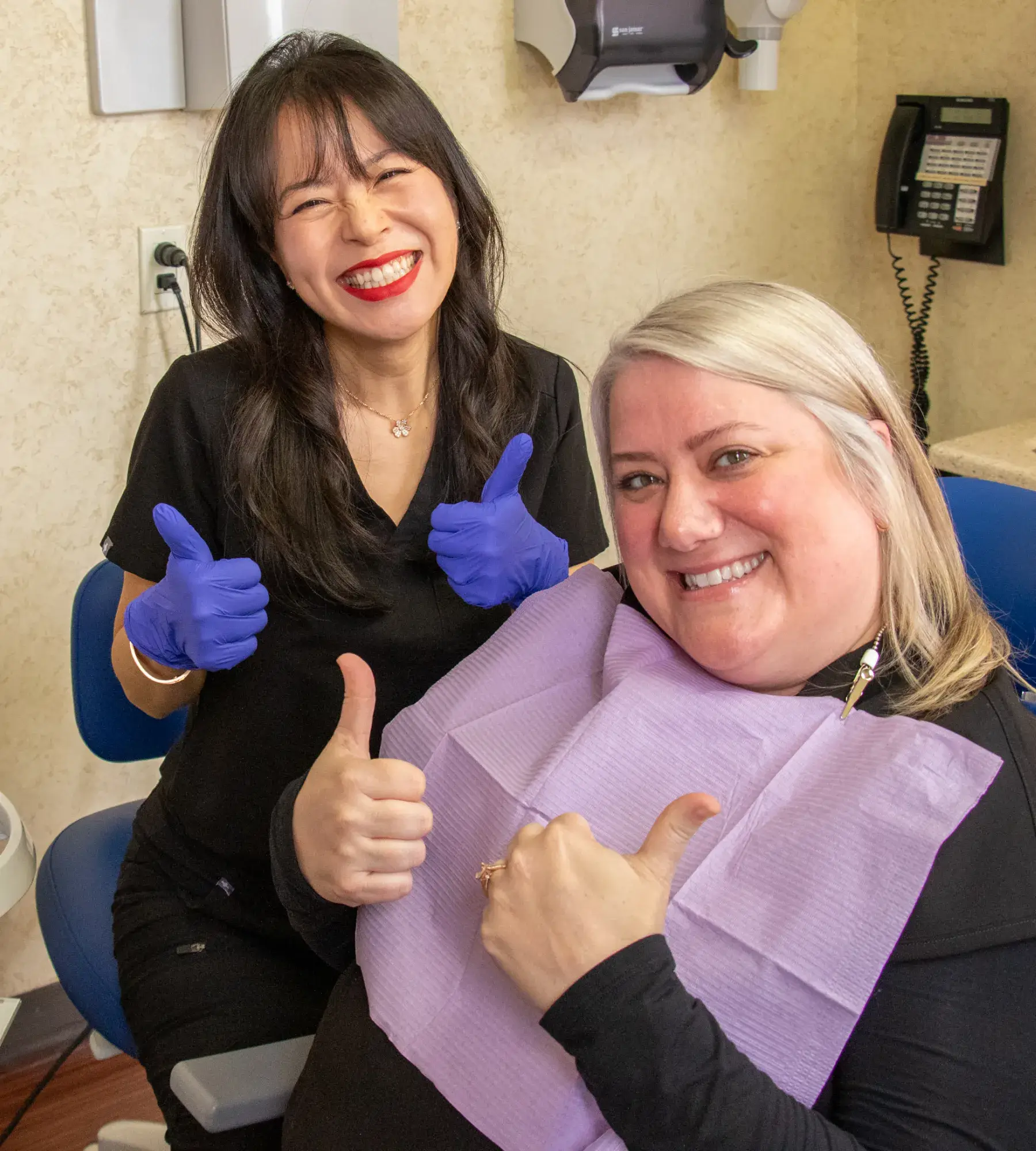 A dental professional and patient smiling and giving thumbs up in a dental office.