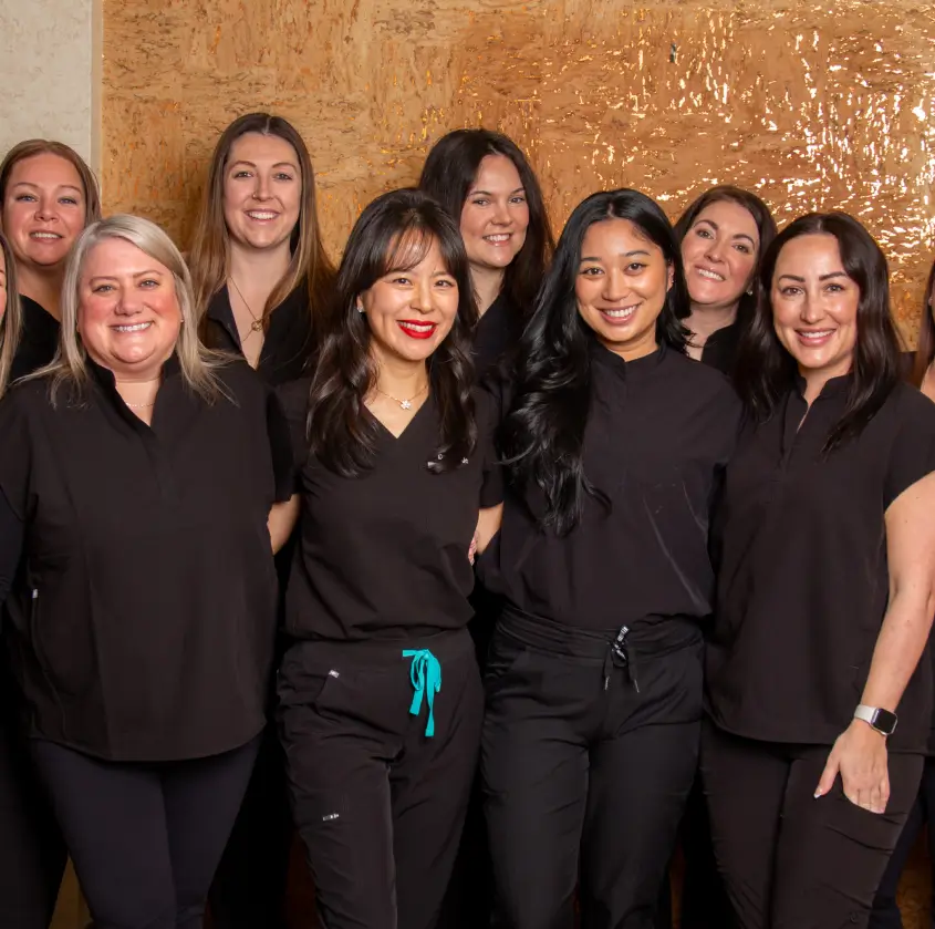 A group of women in matching black outfits pose and smile for a group photo indoors.