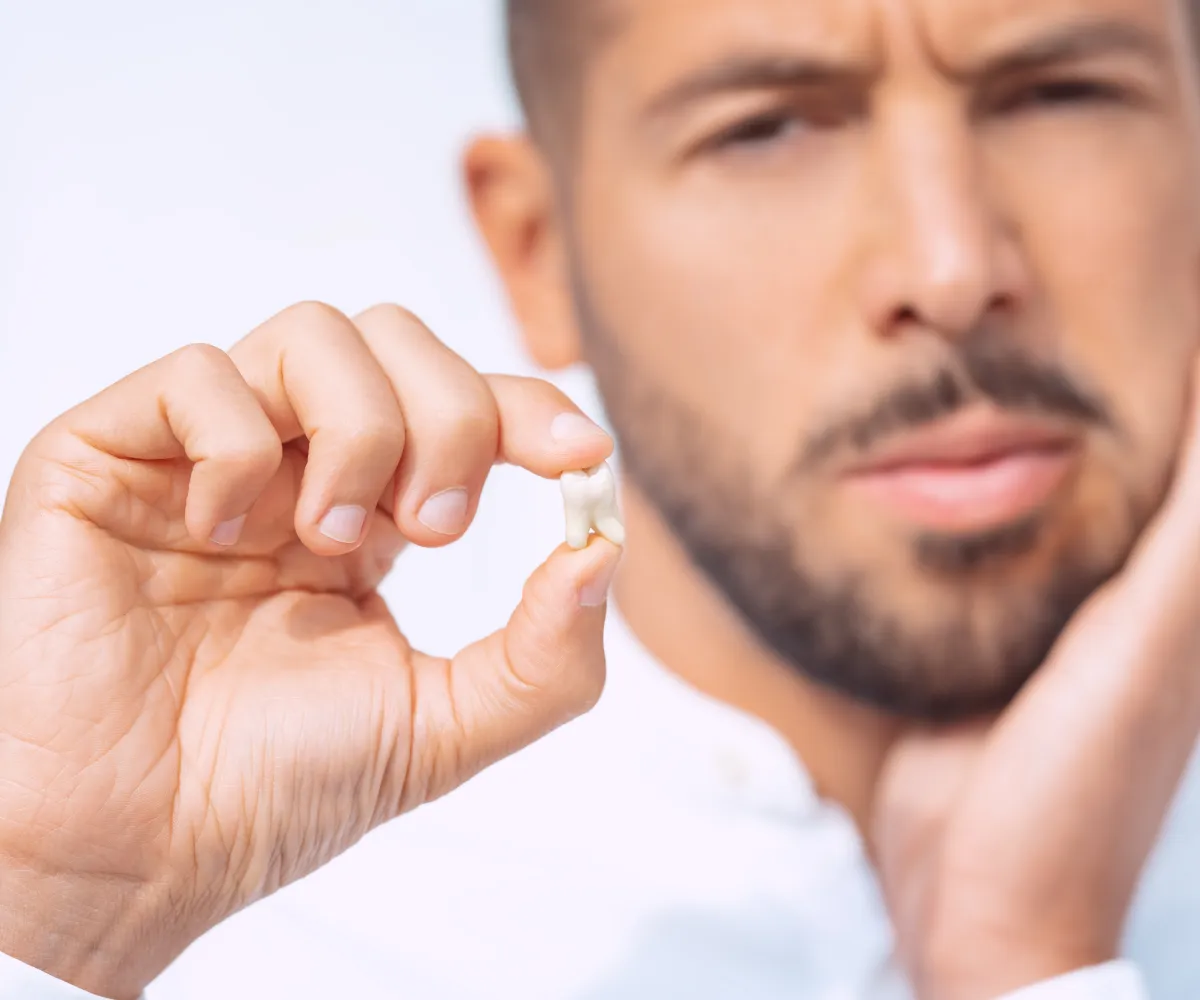 Man holding a tooth, touching his face, possibly indicating toothache.
