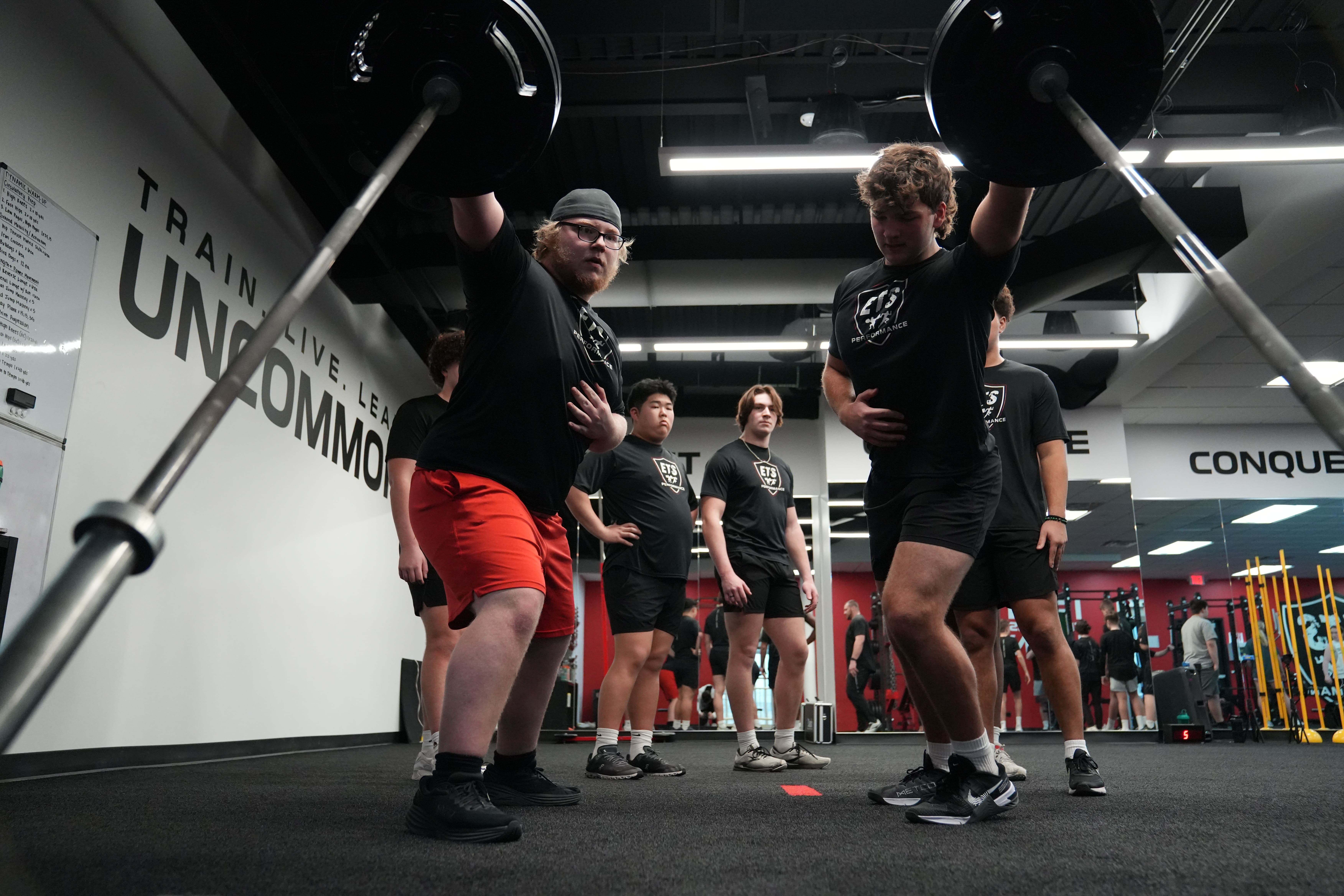 Athletes perform barbell overhead lifts in a group strength and conditioning session at ETS Performance.