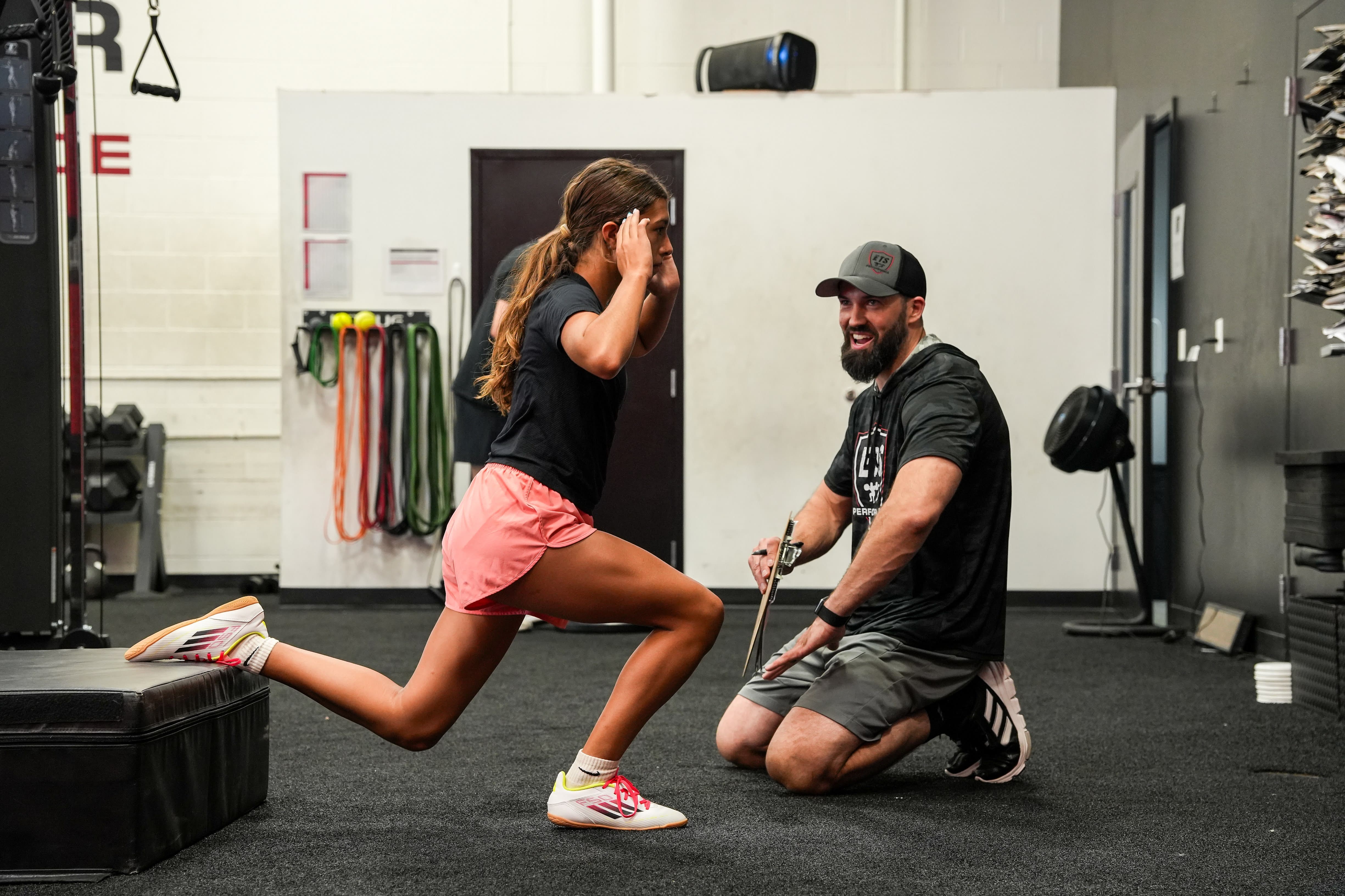 Coach guides an athlete through a forward lunge during one-on-one strength training at ETS Performance.