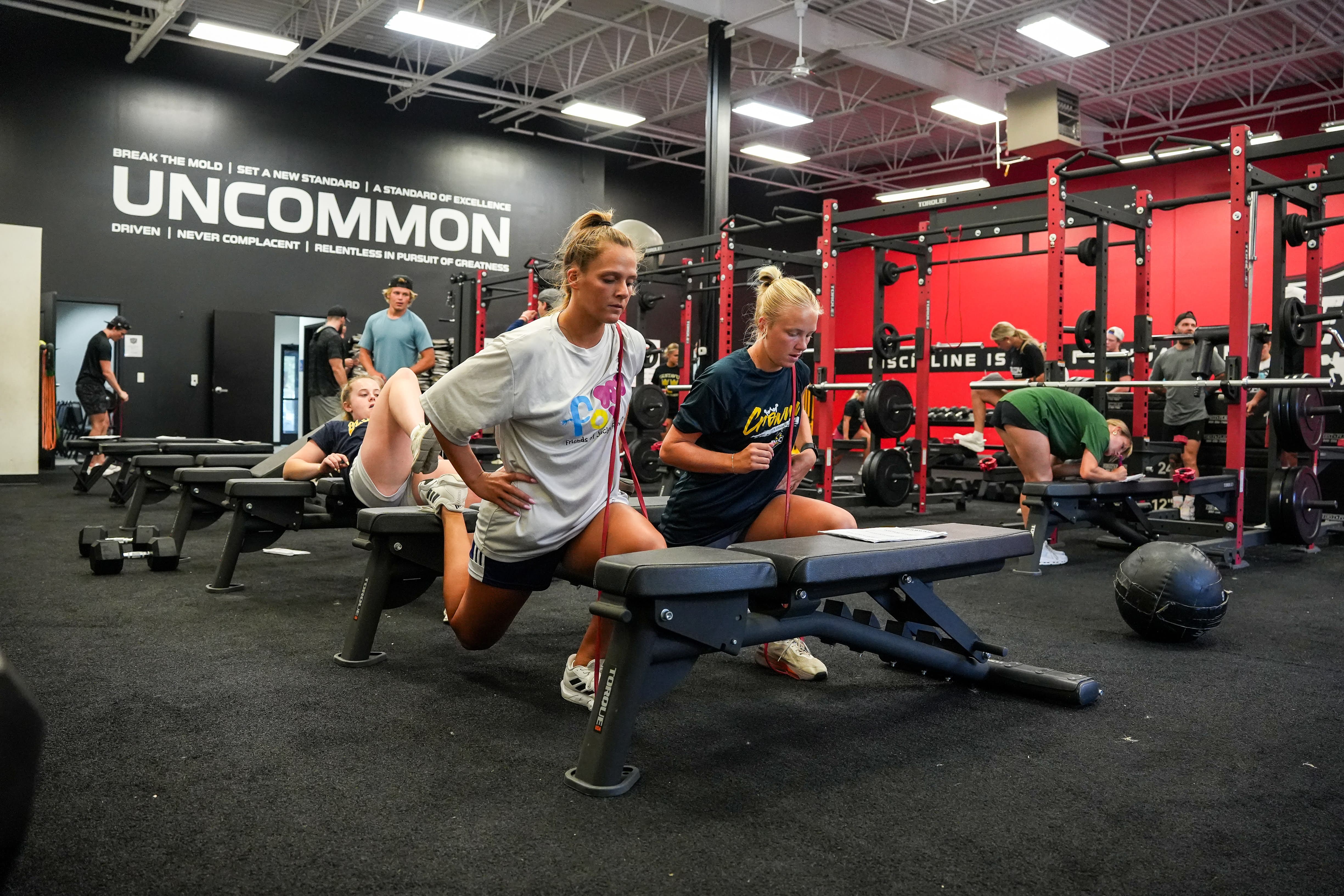 Two athletes practice bench-supported lunges during a team workout in the ETS Performance gym.