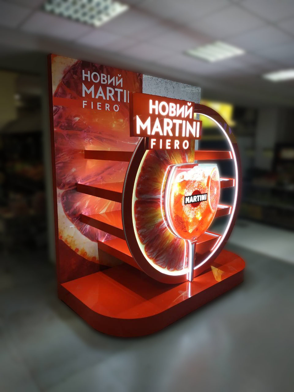 Оголошення з написом Новий Martini Fiero на яскраво-помаранчевій рекламній стійці з зображенням апельсинових часточок і склянки з коктейлем.