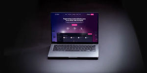 Laptop on a dark surface displaying a website with purple and pink gradient background and white text in the center.