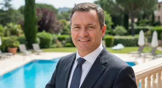 Portrait professionnel de Marc Leblanc, directeur d'hôtel, debout sur une terrasse avec vue sur une piscine et le bâtiment de l'hôtel.