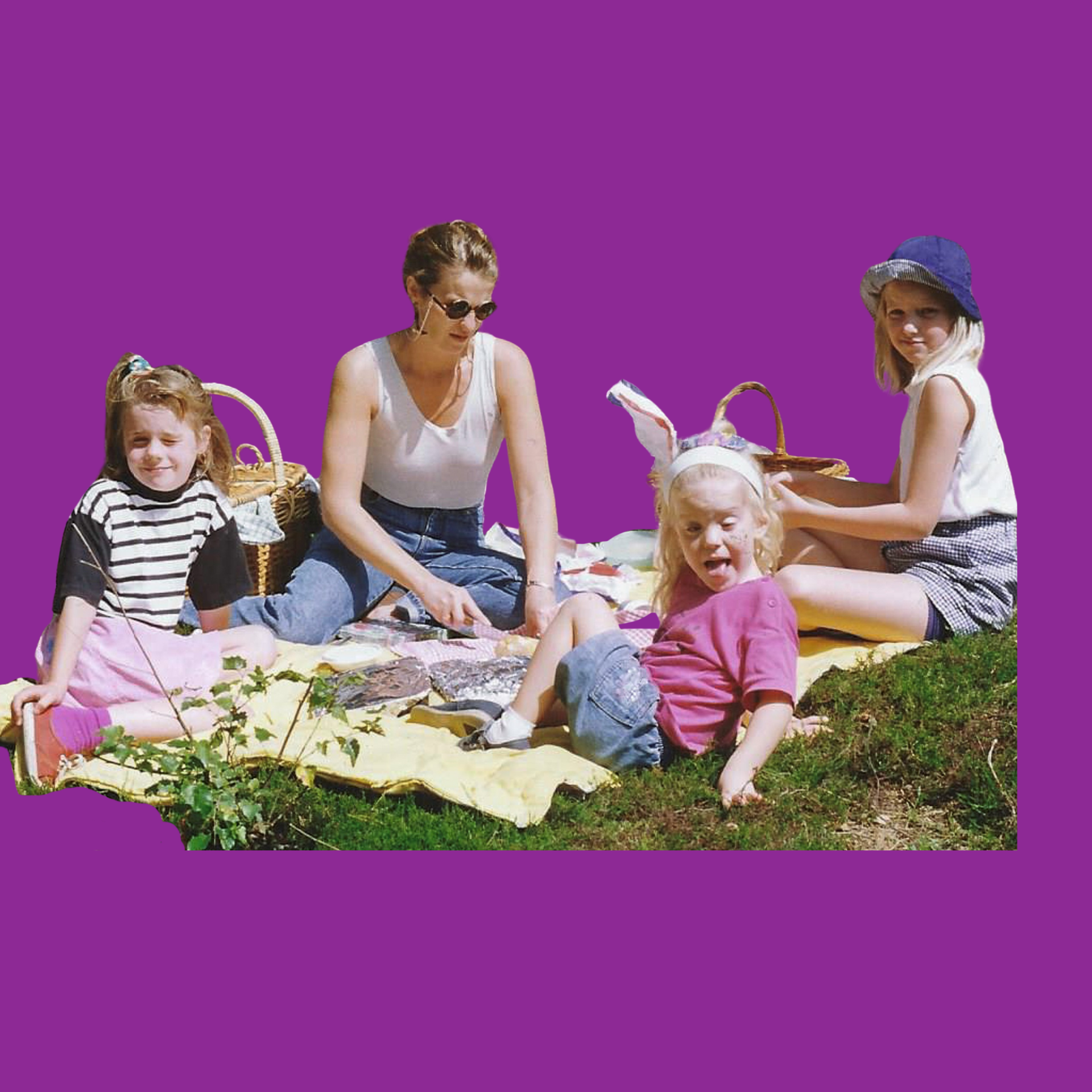 Woman and three children having a picnic outdoors on a yellow blanket with a picnic basket.