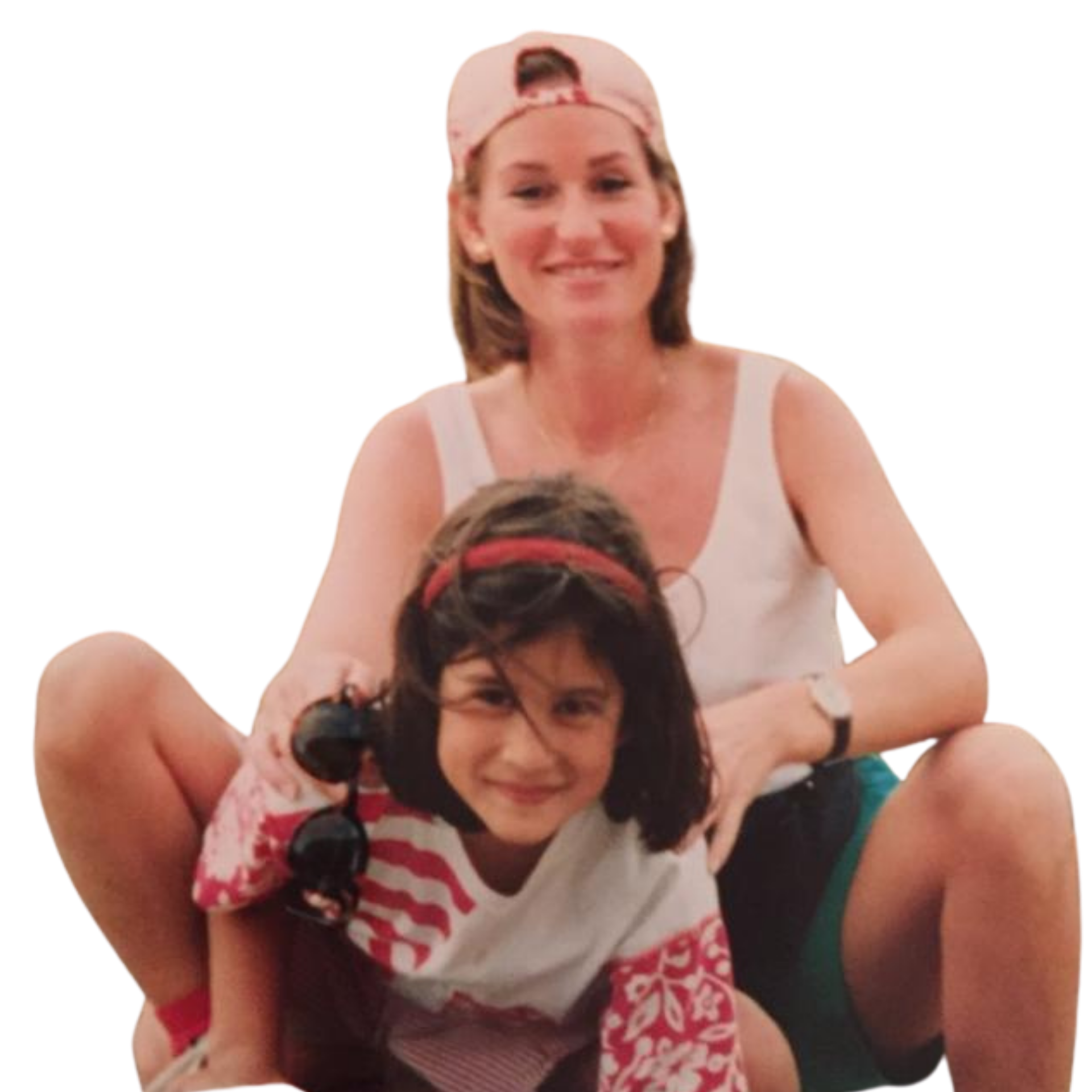 Smiling woman wearing a backward pink cap sitting behind her smiling daughter with a red headband and patterned shirt.