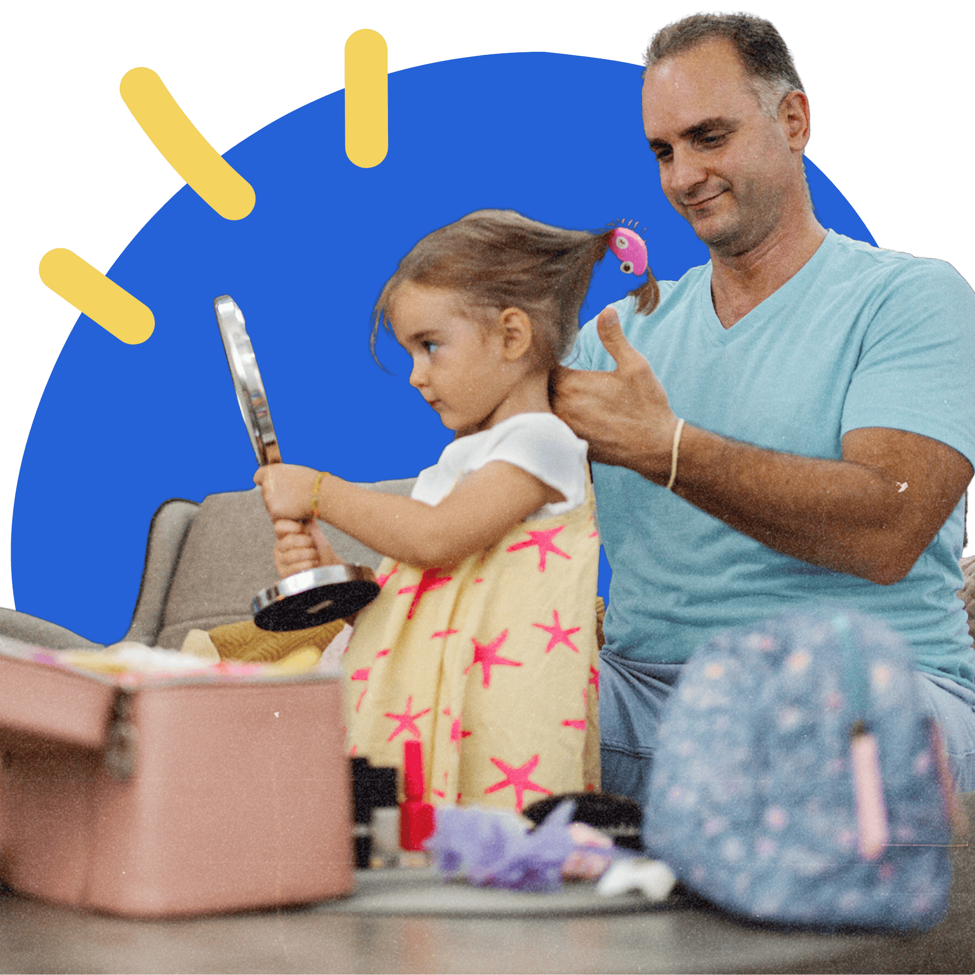 Man styling little girl's hair as she holds a mirror, seated at a table with makeup items.