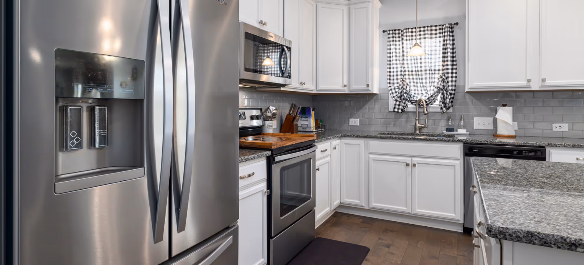 Modern kitchen with stainless steel refrigerator, oven, microwave, and dishwasher installed in white cabinetry.