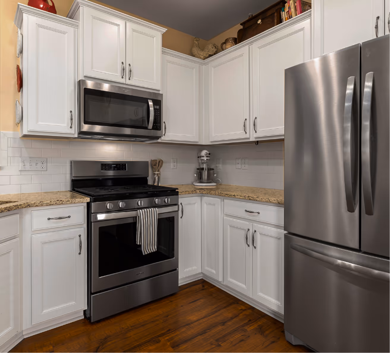 Modern kitchen with stainless steel refrigerator, gas range, microwave, and white cabinets with granite countertops.