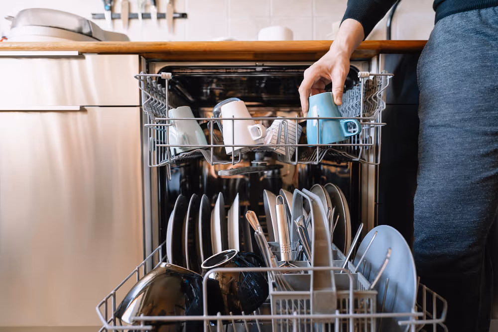 Person loading cups into open dishwasher rack