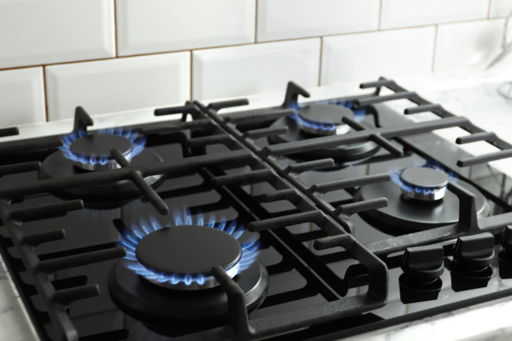 Gas cooktop with blue flames burning on all burners in a modern kitchen