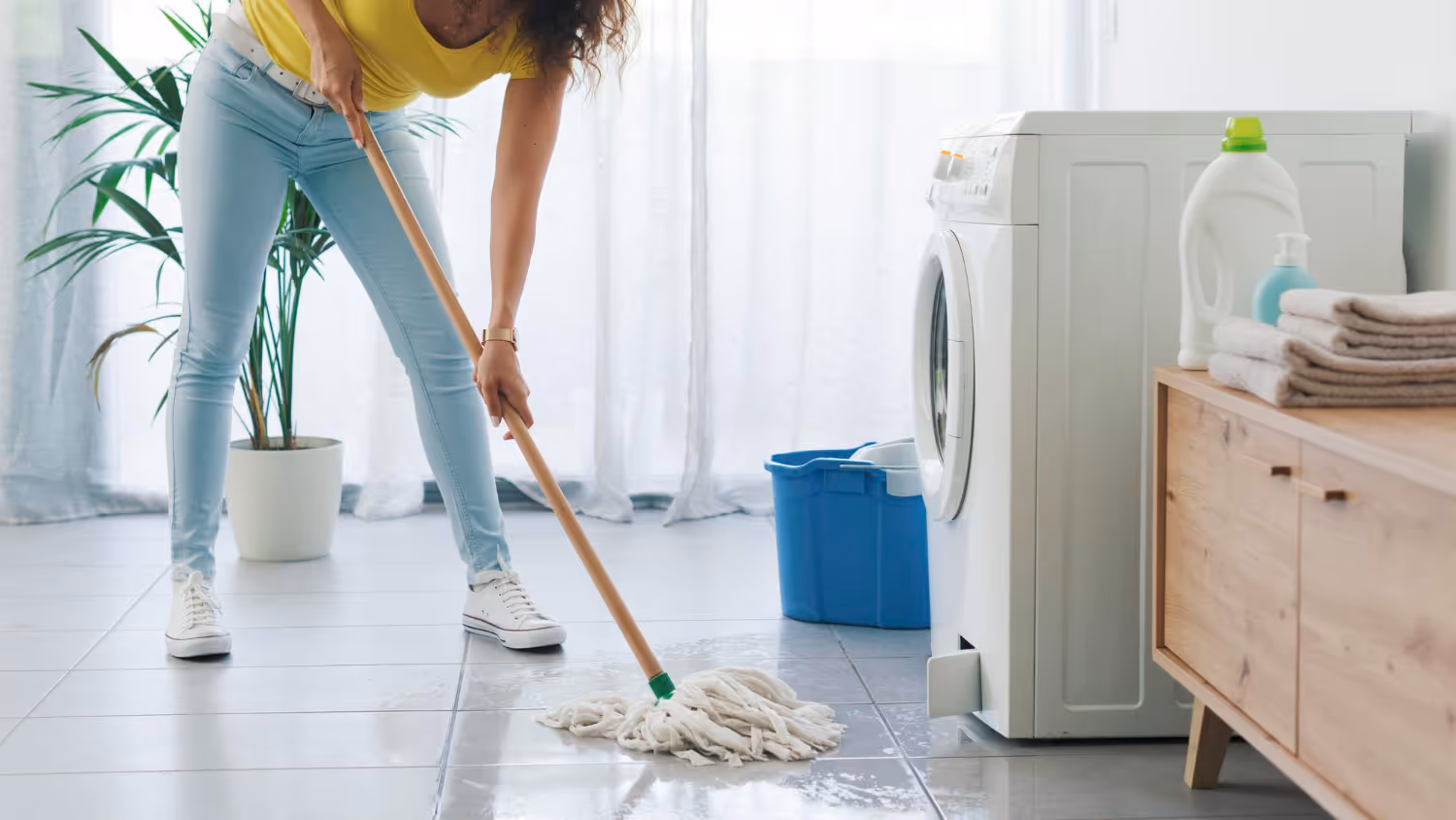 Woman cleaning water from floor after washing machine leak in laundry room