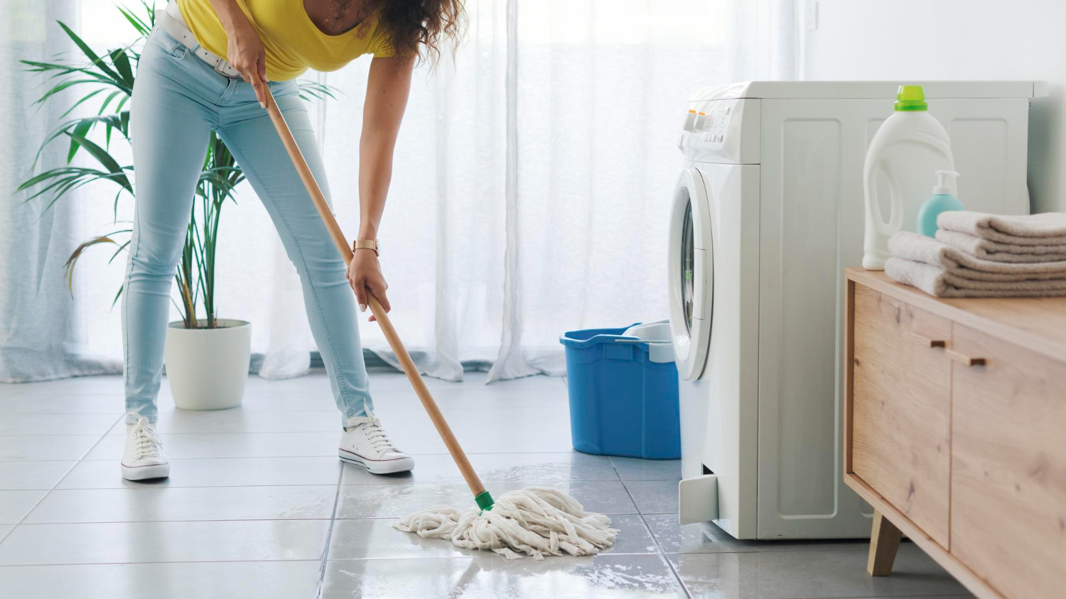 Woman cleaning water from floor after washing machine leak in laundry room
