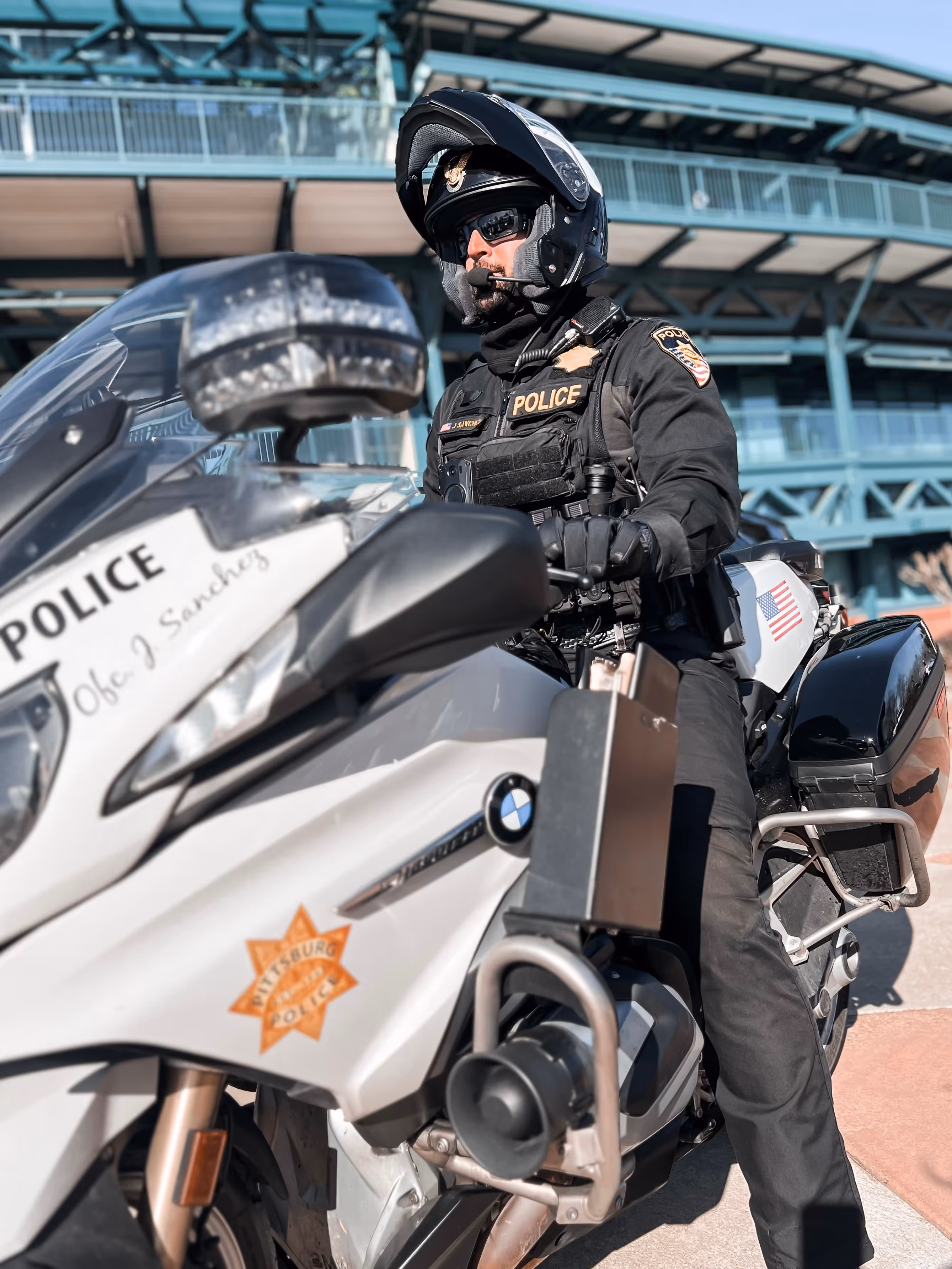 Police officer in black uniform and helmet sitting on a white police motorcycle with Pittsburgh Police badge and American flag.