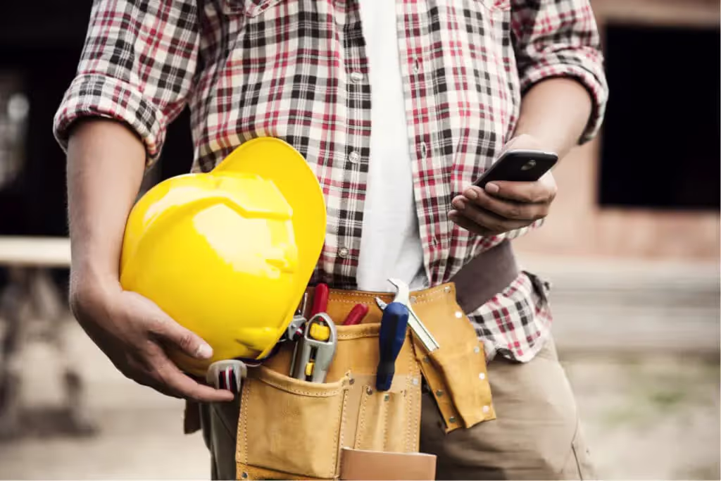 Construction worker holding hardhat using phone to run calculations on job site