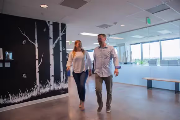 Two team members walk by Engine entrance with glass windows and tree mural in background