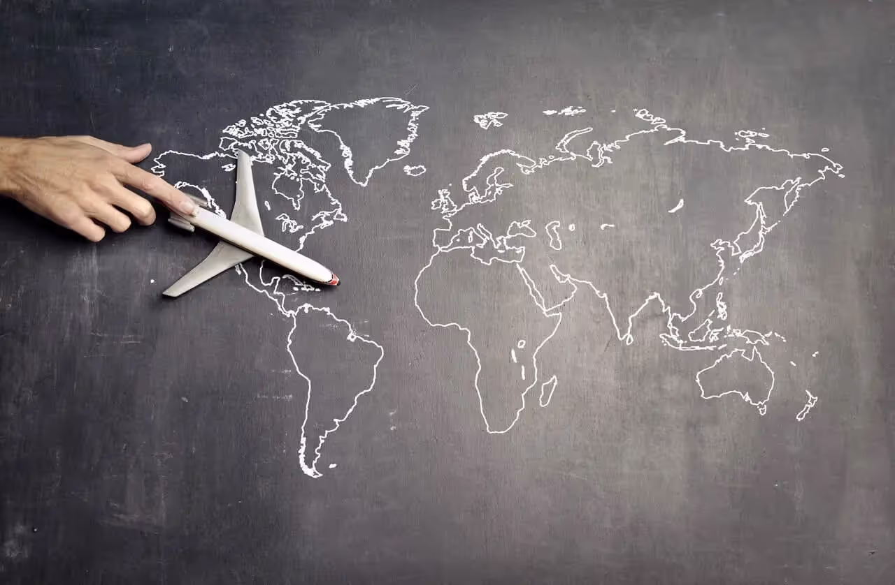 Person holding airplane over world map drawn on chalkboard