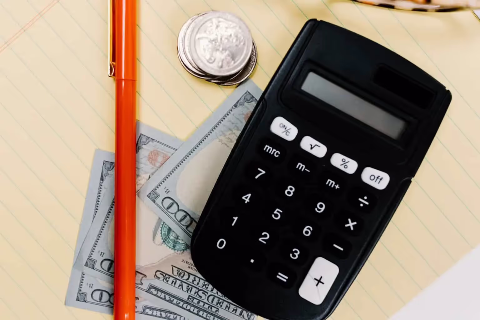 Calculator, dollar bills, quarters, and red pen on a desk